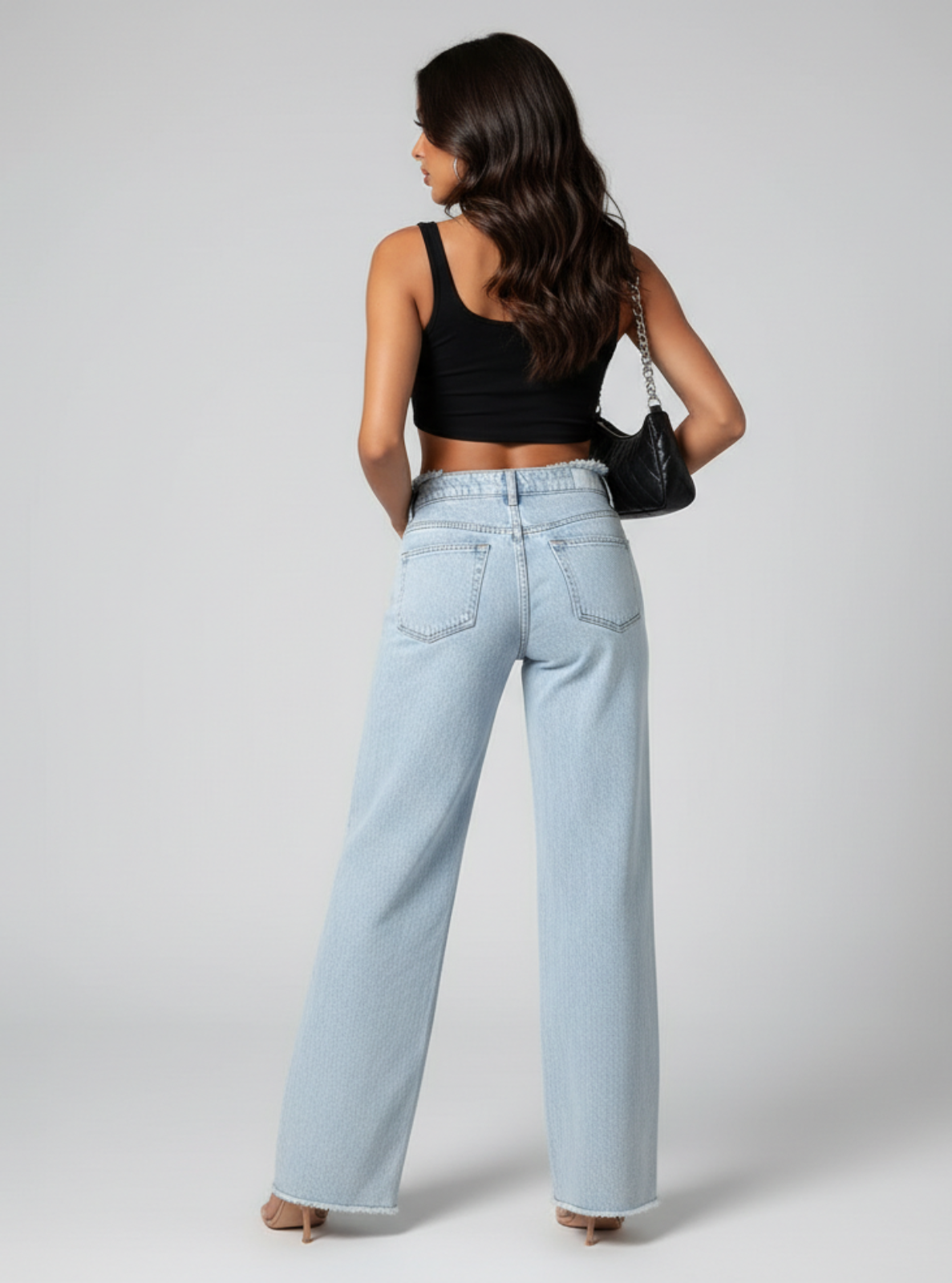 Woman wearing light blue jeans and a black top on a plain background