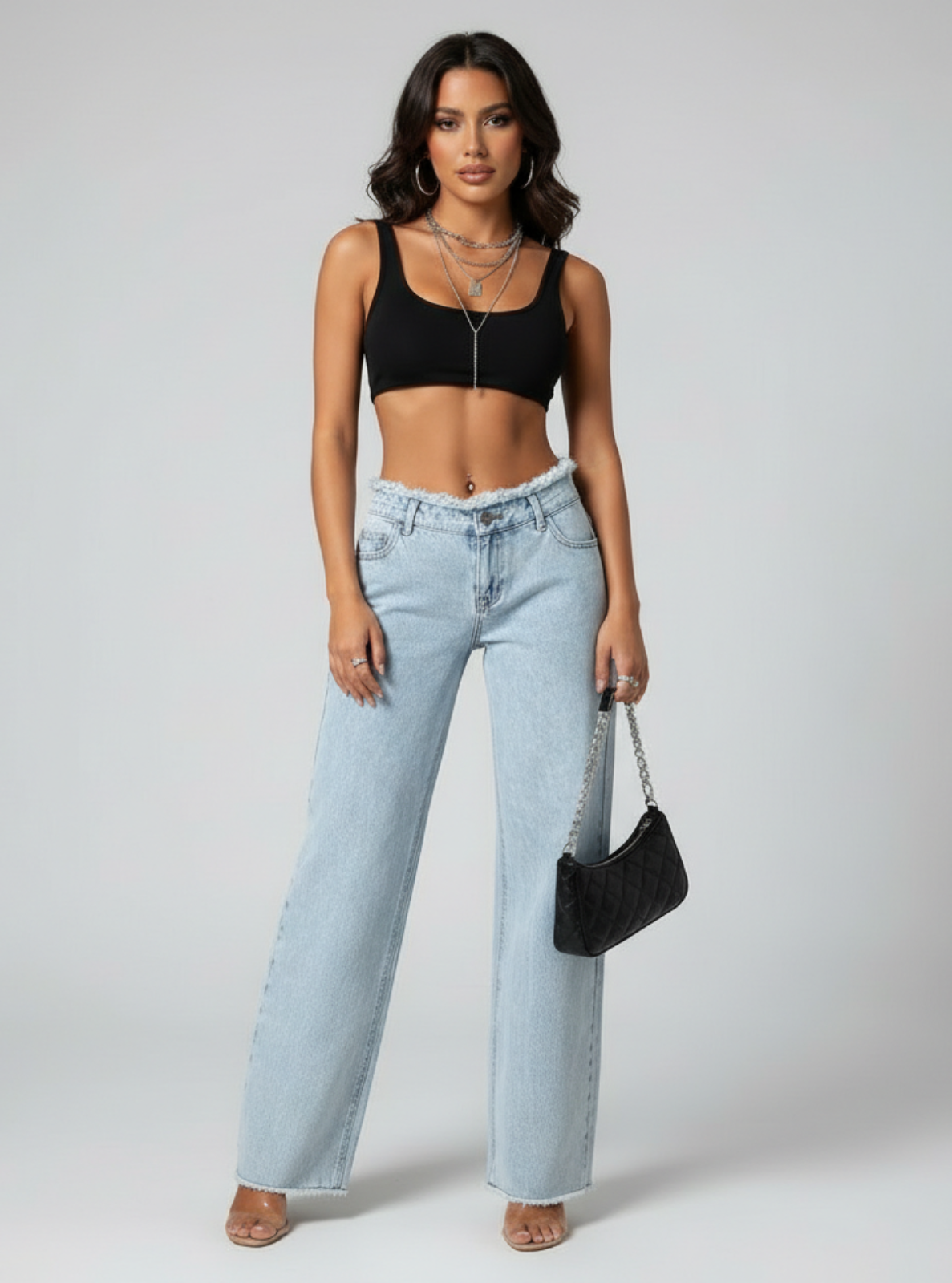 Woman wearing a black crop top and light blue jeans, holding a black handbag on a white background