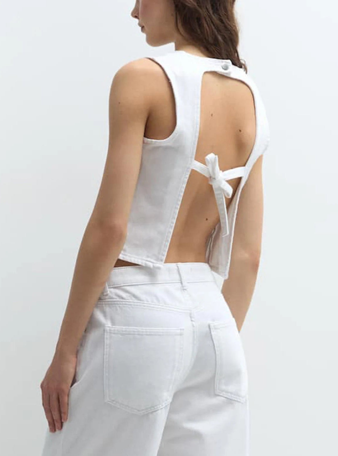 Person wearing a white sleeveless top with cut-out design on a plain background