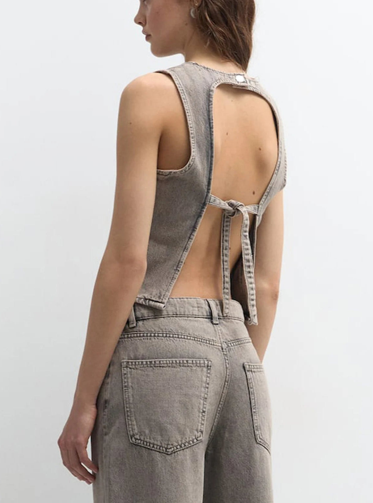 Person wearing a gray denim jumpsuit with open back on a white background