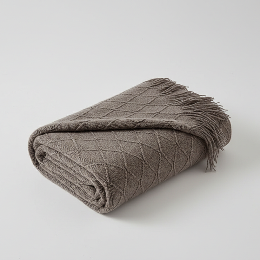 Folded brown blanket with diamond pattern and fringe on a light gray background