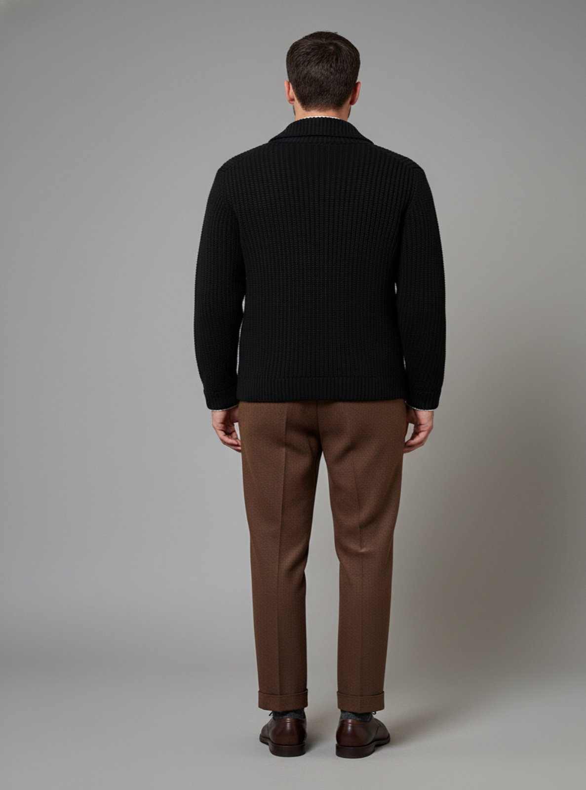 Man wearing a black sweater and brown pants against a gray background