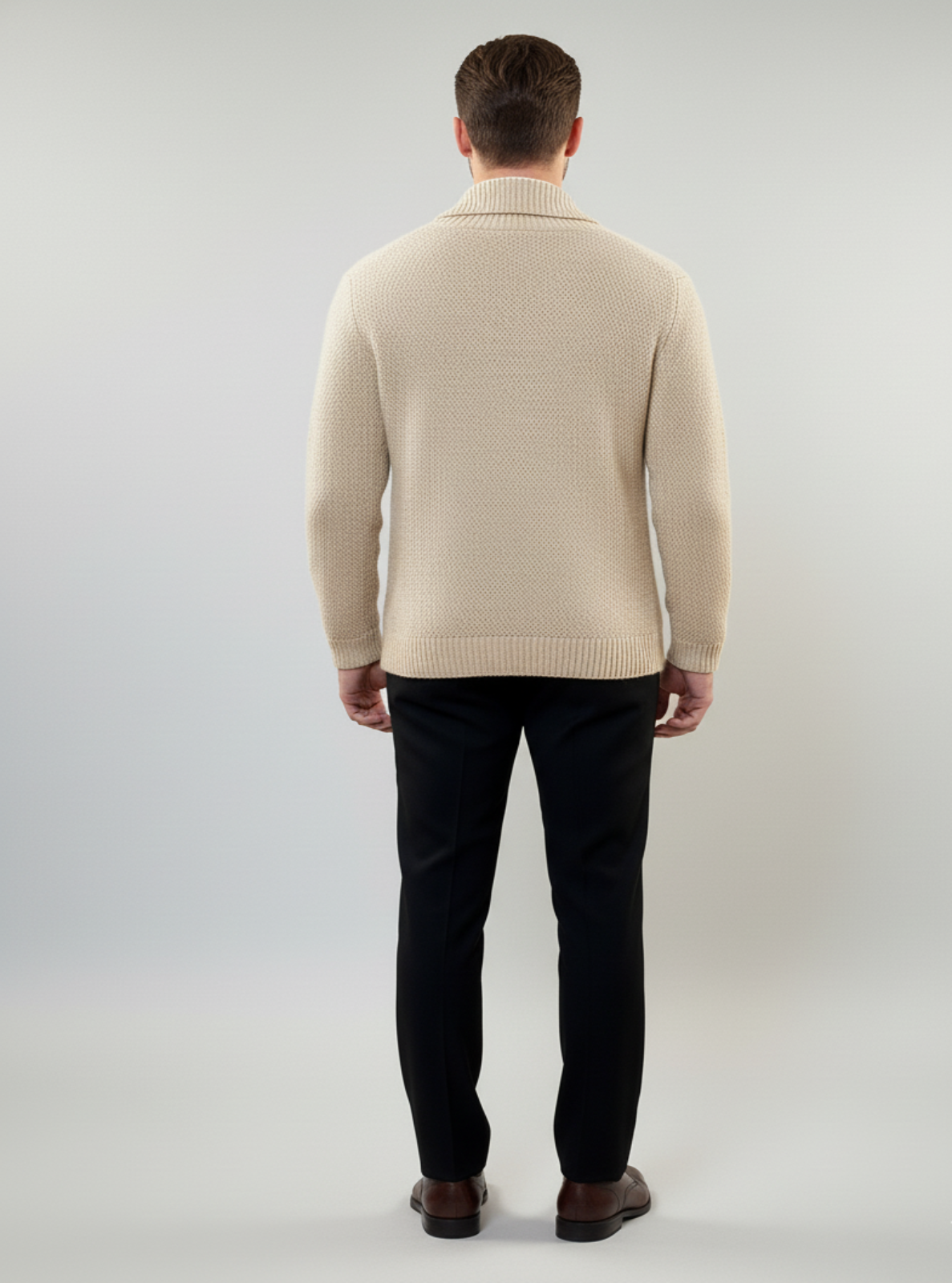 Man wearing a beige sweater and black pants on a gray background