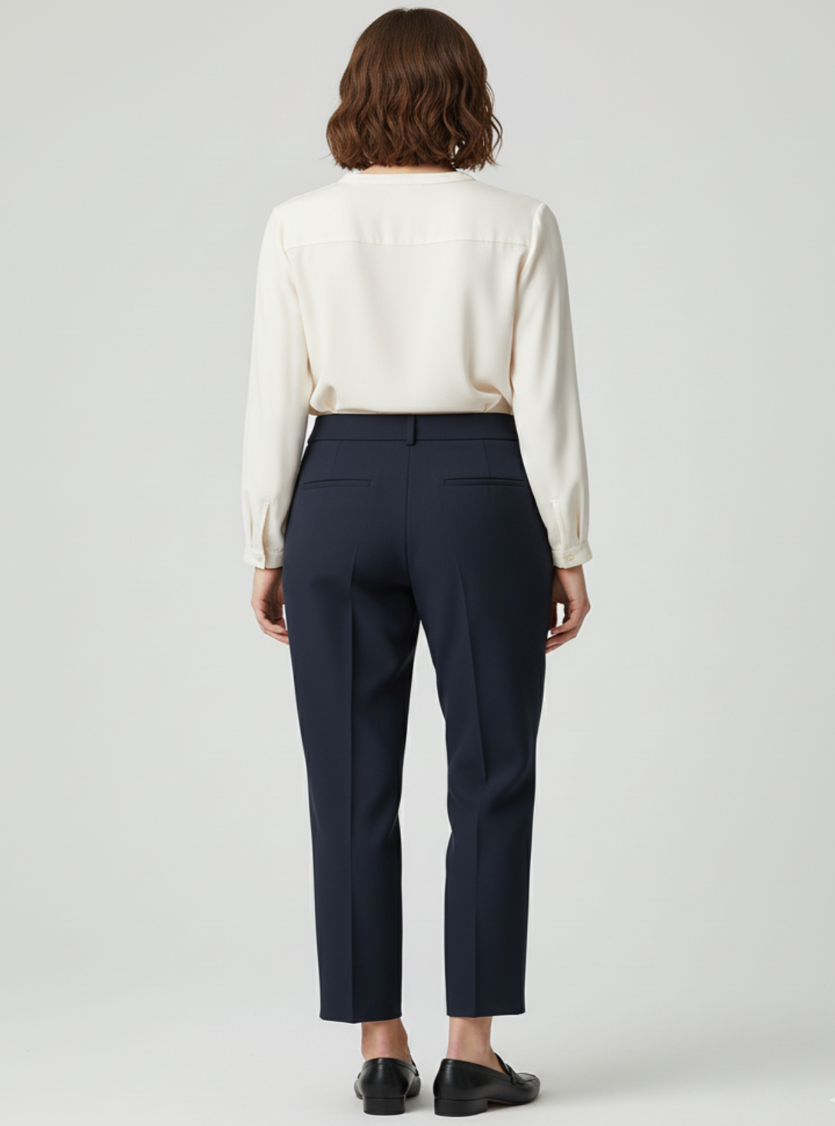 Person wearing a white blouse and navy pants on a plain background