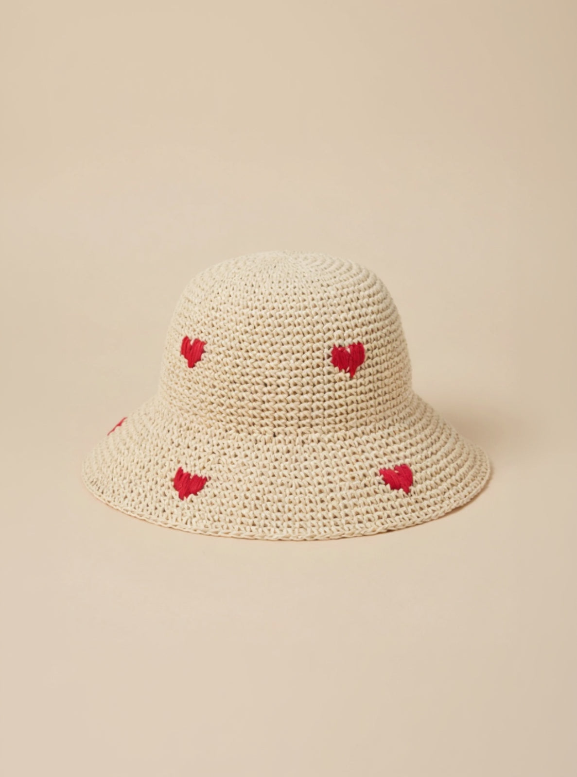 Beige woven hat with red heart patterns on a beige background
