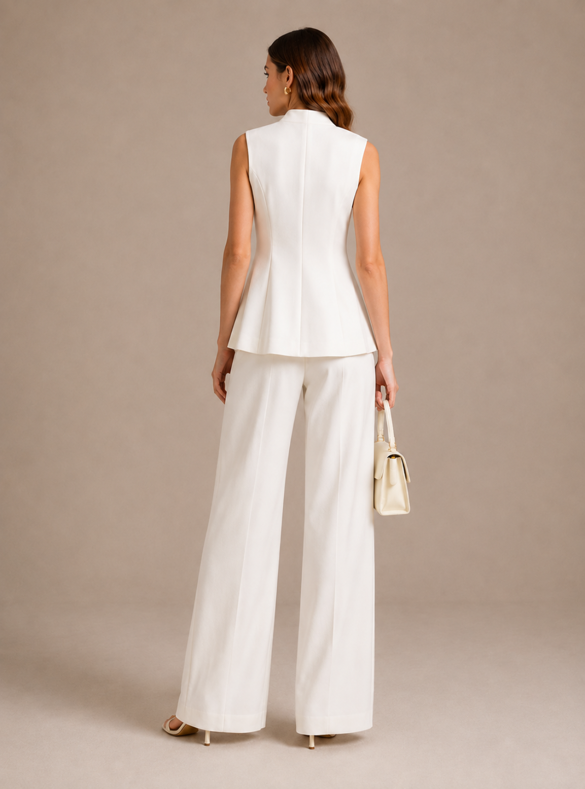 A woman is shown from the back wearing a white sleeveless peplum-style vest and matching white wide-leg trousers, holding a small cream handbag against a plain beige studio background.