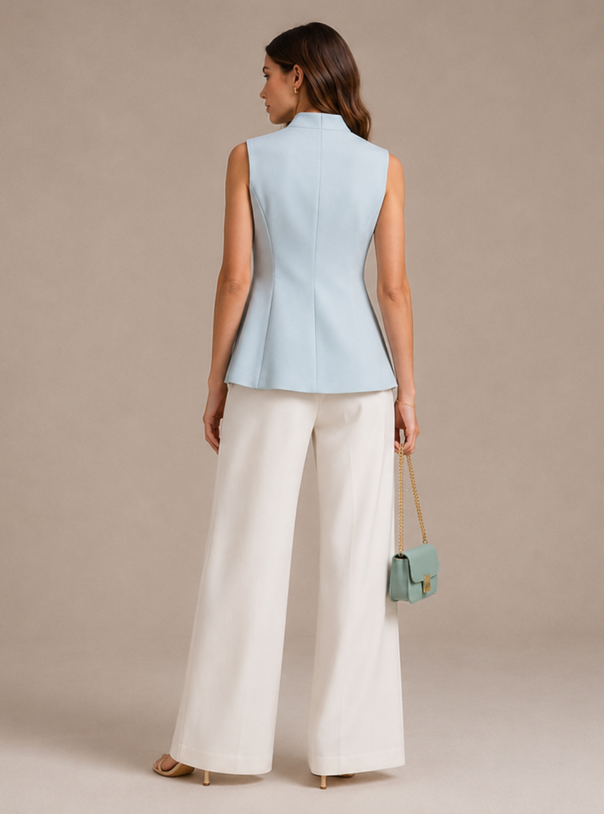 A woman is shown from the back wearing a light blue sleeveless structured vest and white wide-leg trousers, holding a small mint green handbag against a neutral beige studio background.
