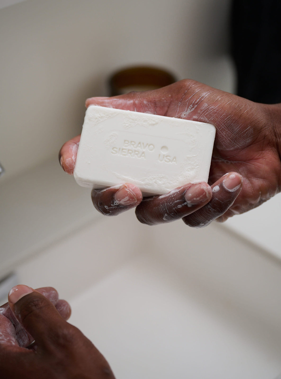 Person holding a bar of soap above a sink with a faucet in the background
