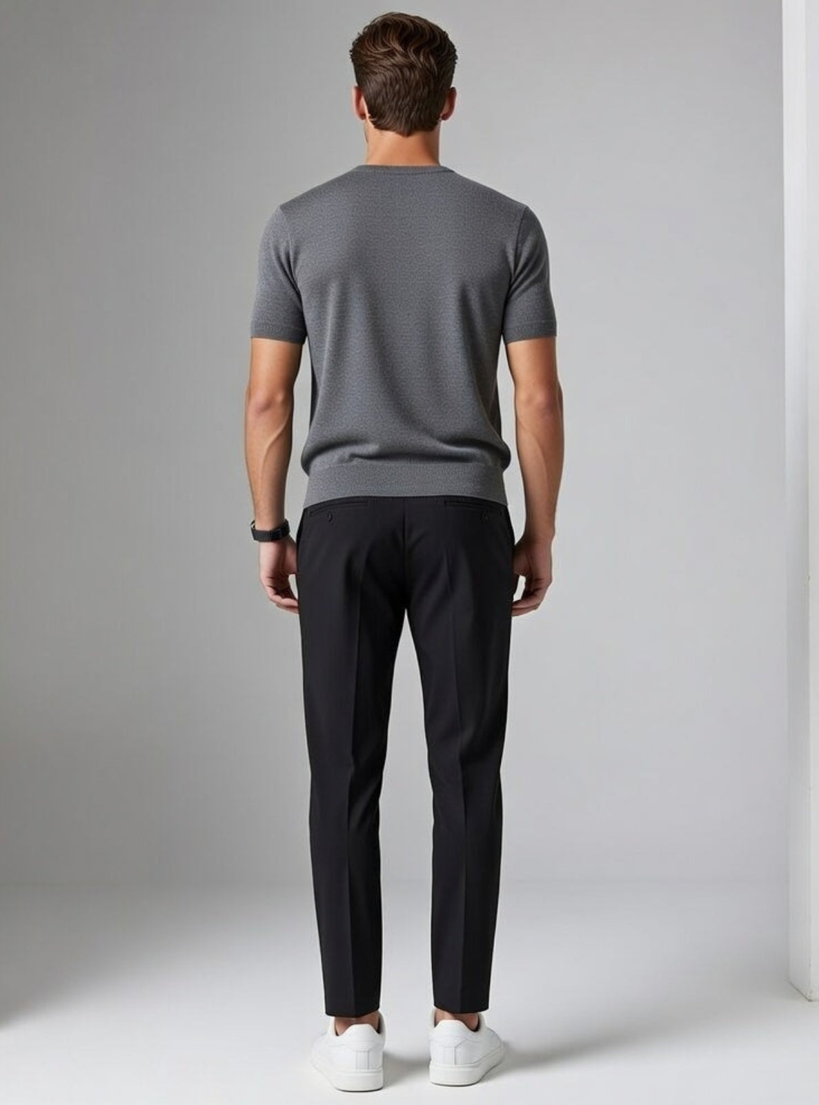 Man wearing a gray t-shirt and black pants standing against a plain background