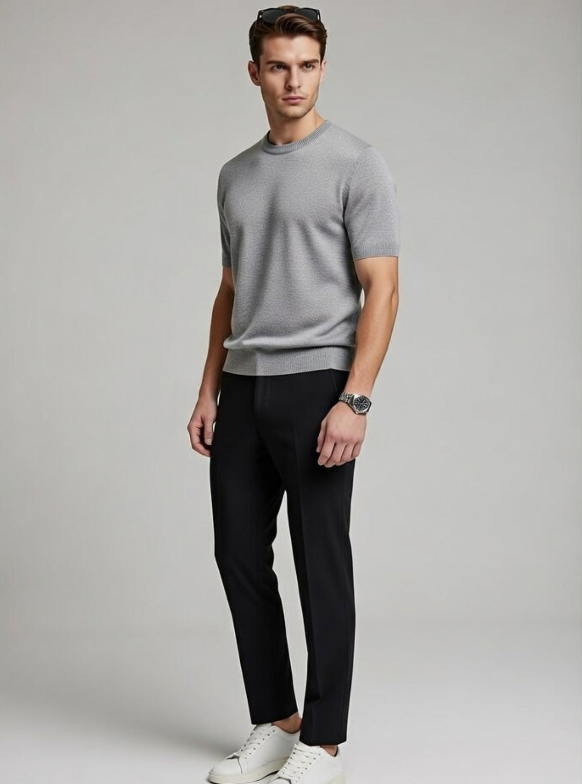 Man wearing a gray t-shirt, black pants, and white sneakers on a plain background