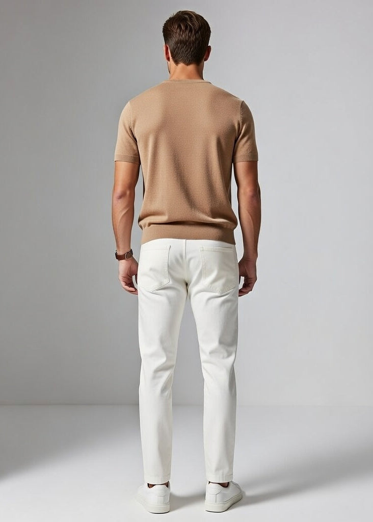 Man wearing a brown sweater and white pants standing against a plain background