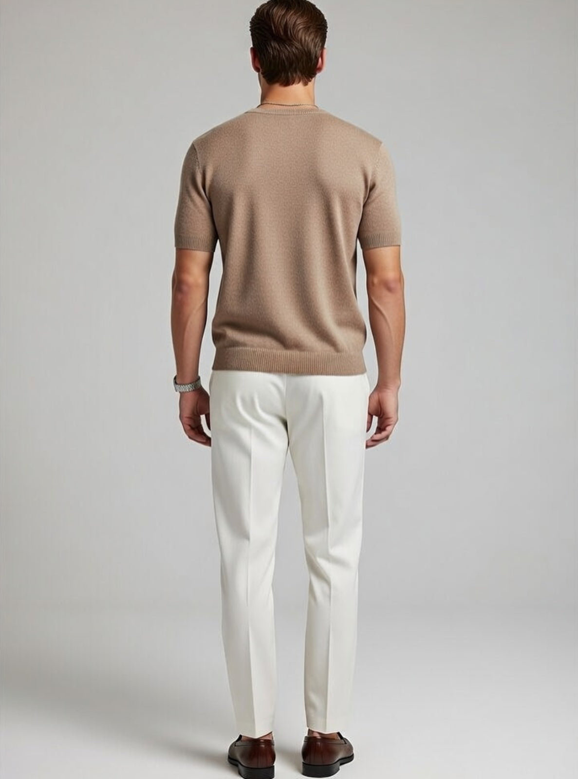 Man wearing a brown sweater and white pants on a plain background