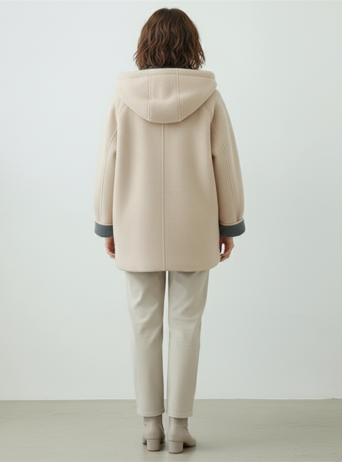 Person wearing a beige coat with a hood on a plain background