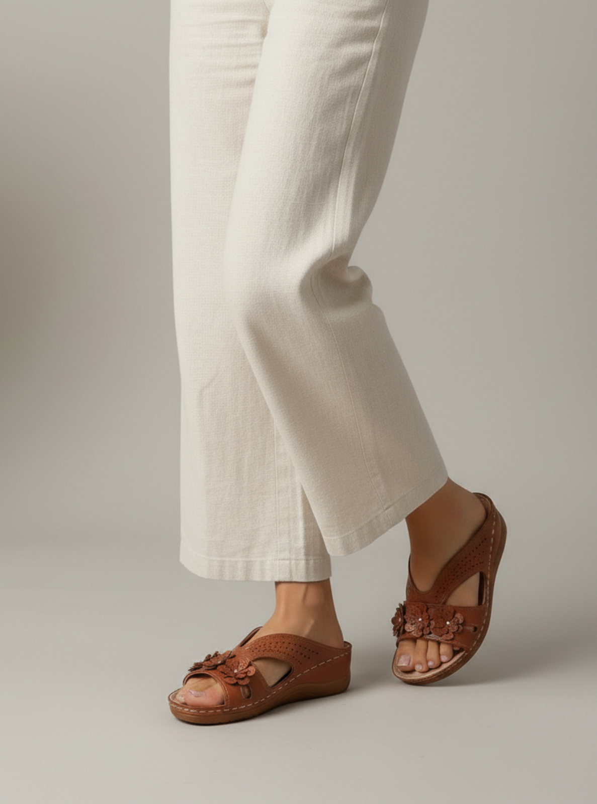 Brown sandals worn with white pants on a neutral background