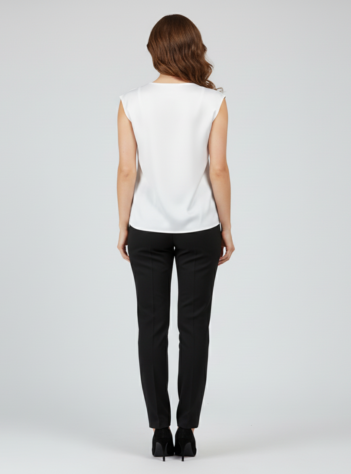 Woman wearing a white sleeveless top and black pants on a gray background