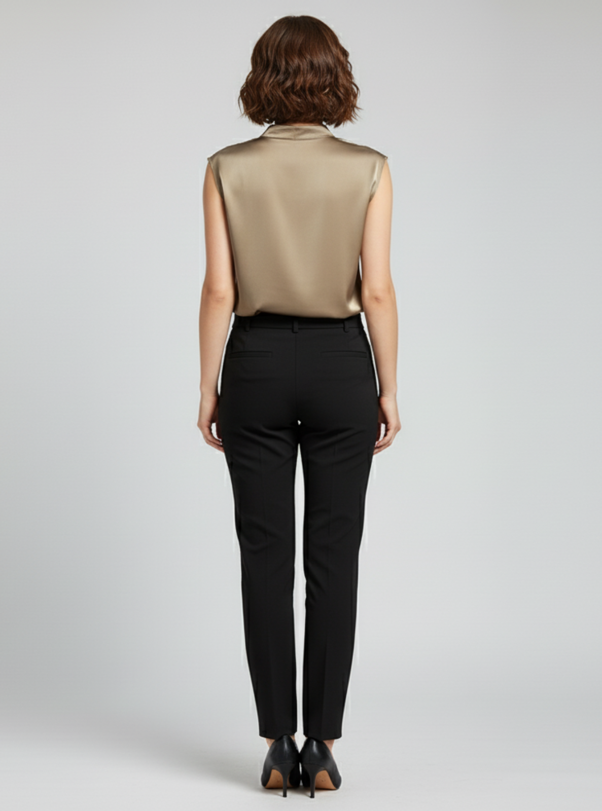 Woman wearing a beige sleeveless top and black pants on a plain background