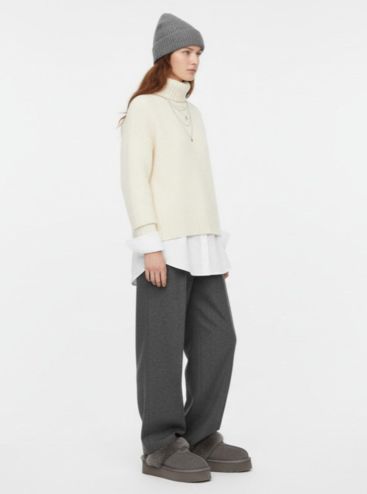 Person wearing a cream sweater, gray pants, and a gray beanie on a white background