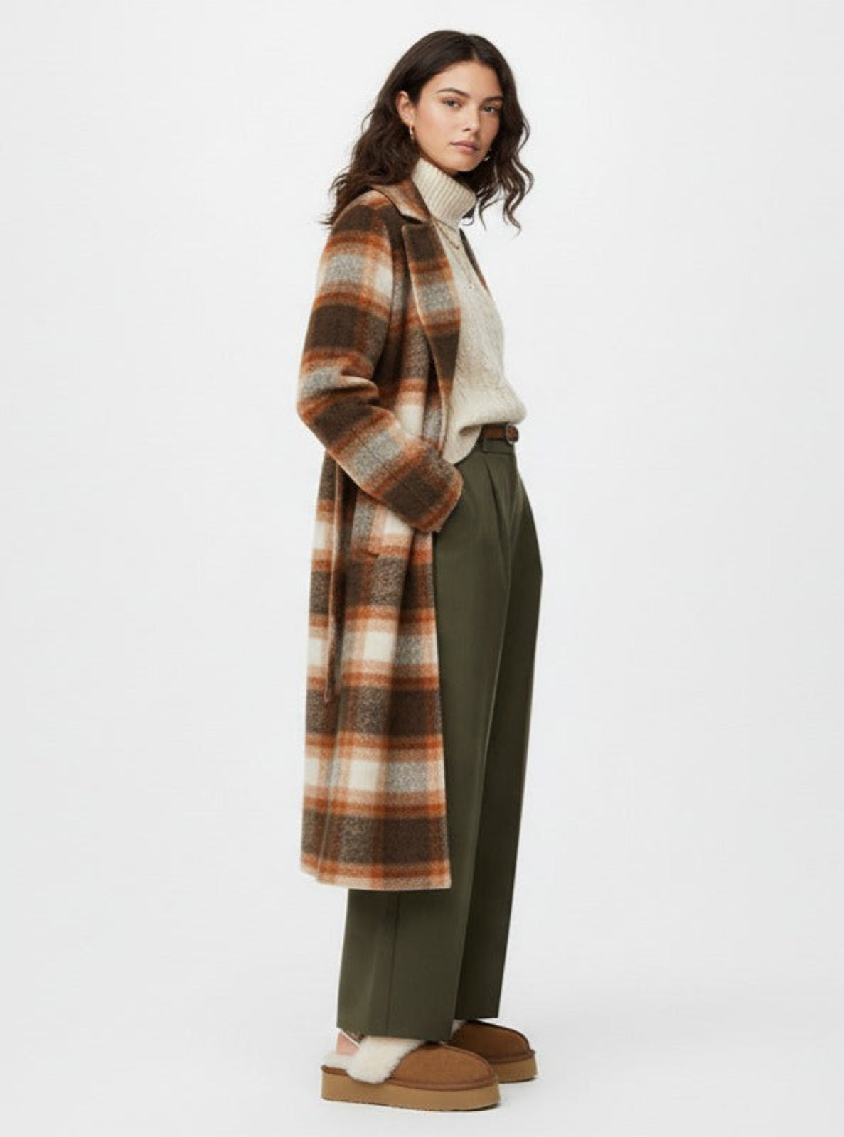 Woman wearing a plaid coat, white sweater, green pants, and brown shoes on a white background