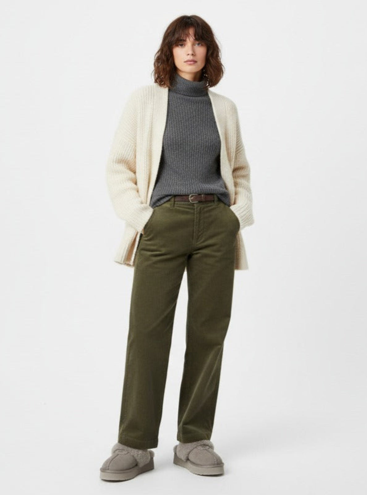 Woman wearing a cream cardigan, gray sweater, green pants, and gray shoes on a white background