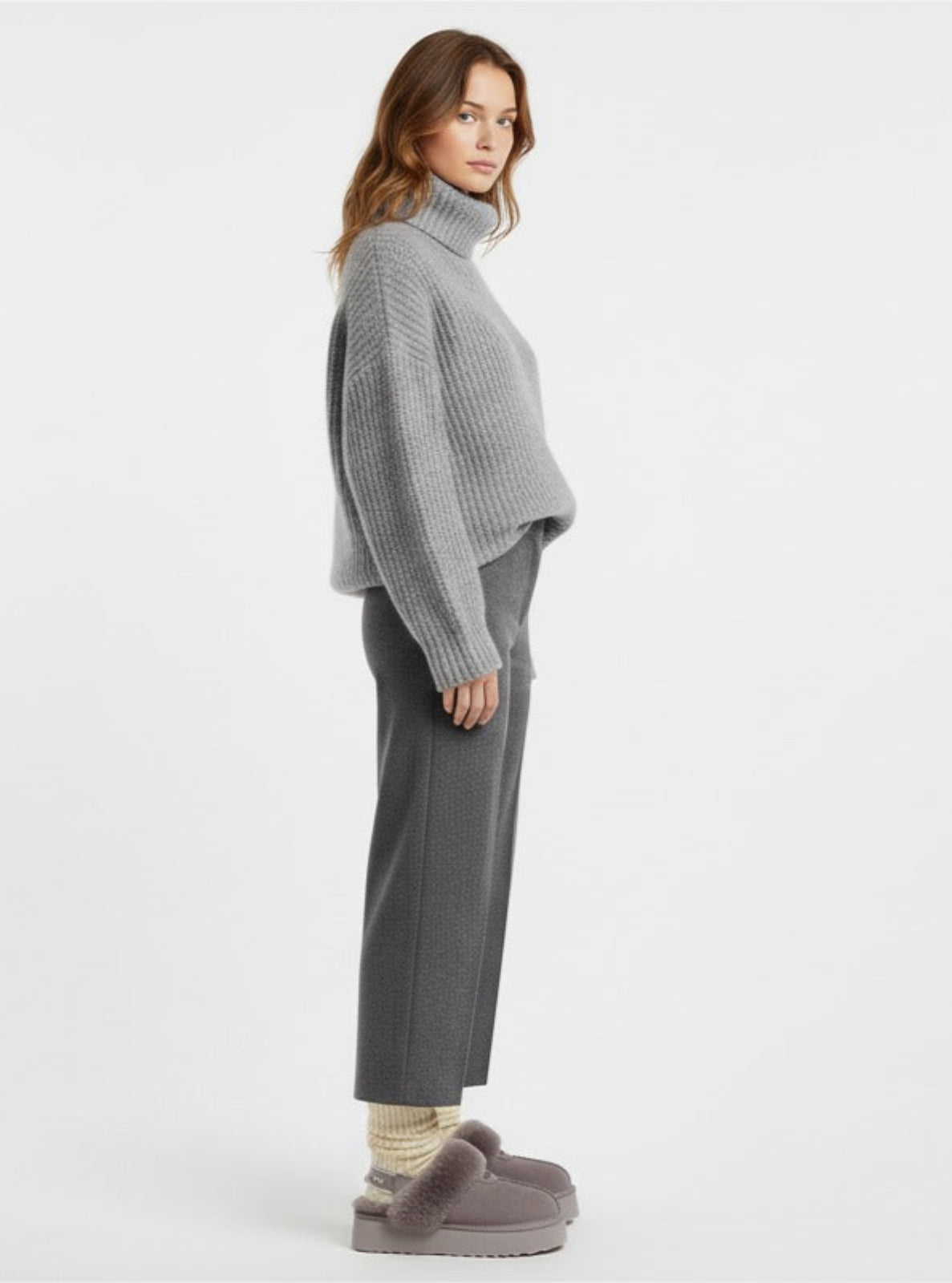 Woman wearing a gray turtleneck sweater and pants with gray slippers on a white background