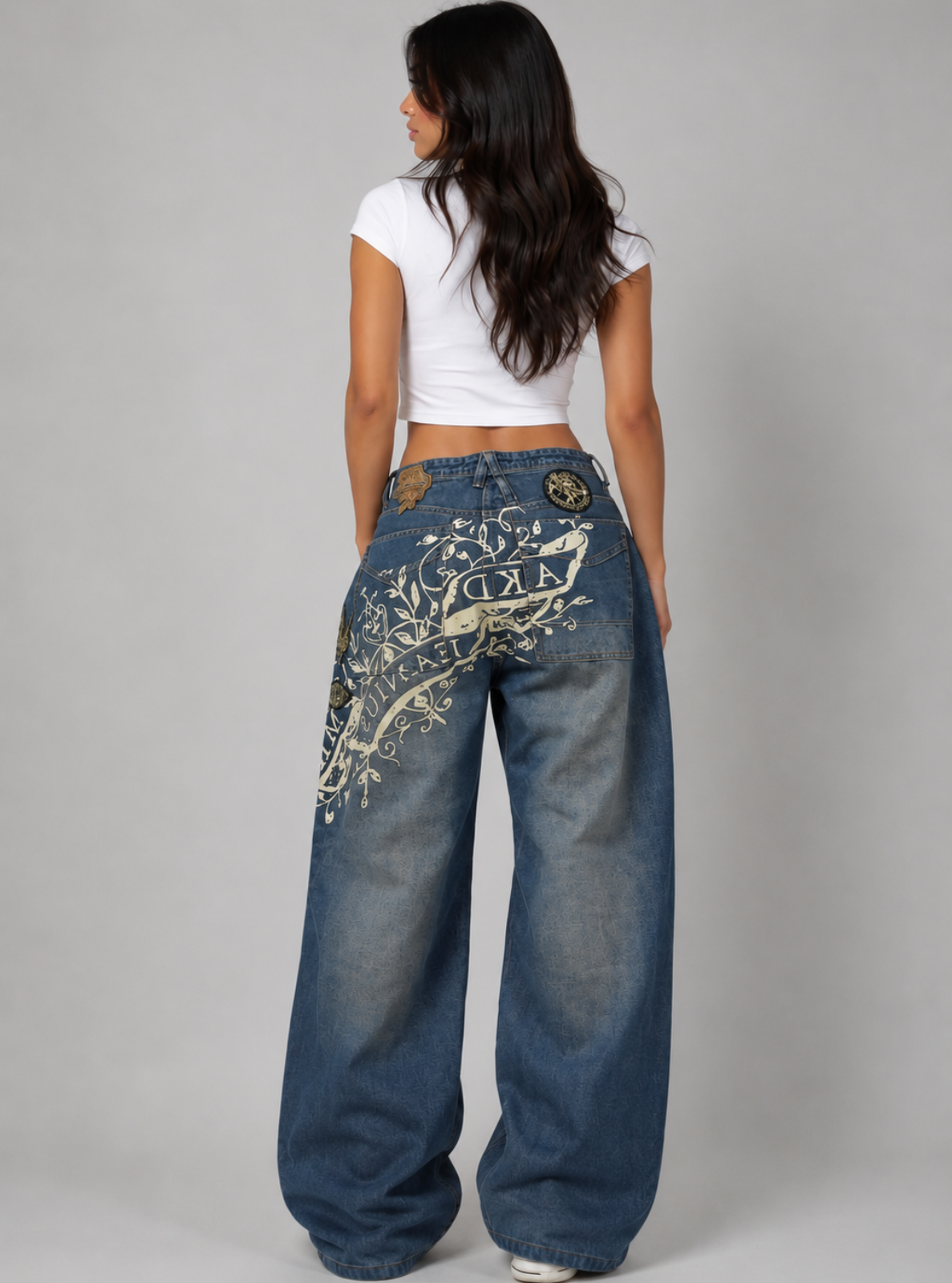 Woman wearing blue jeans with a floral design on the back, standing against a plain background
