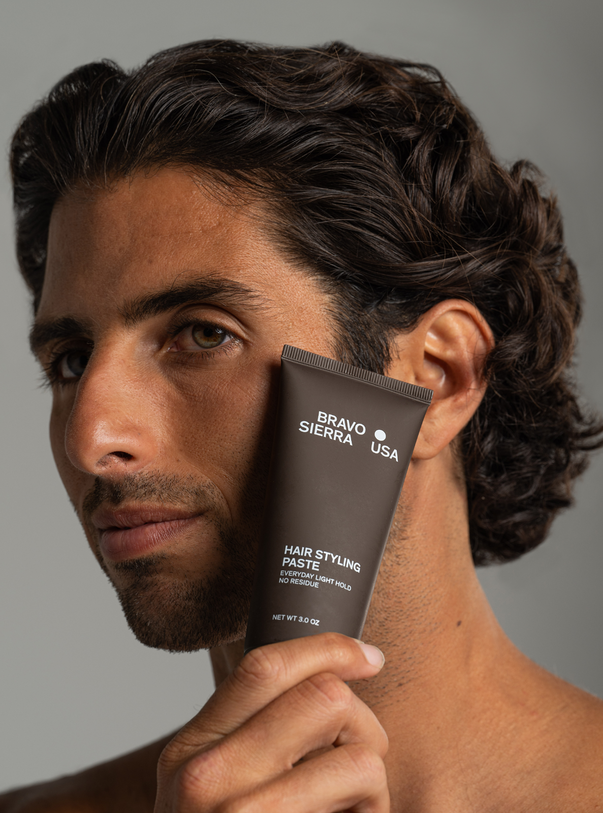 Man holding a bottle of hair styling paste against a gray background
