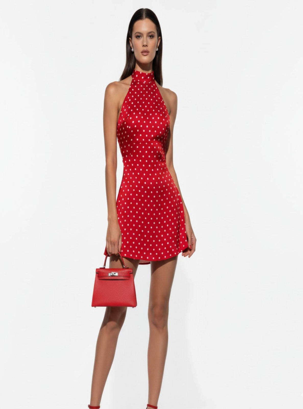 Woman wearing a red polka dot dress holding a matching handbag on a white background