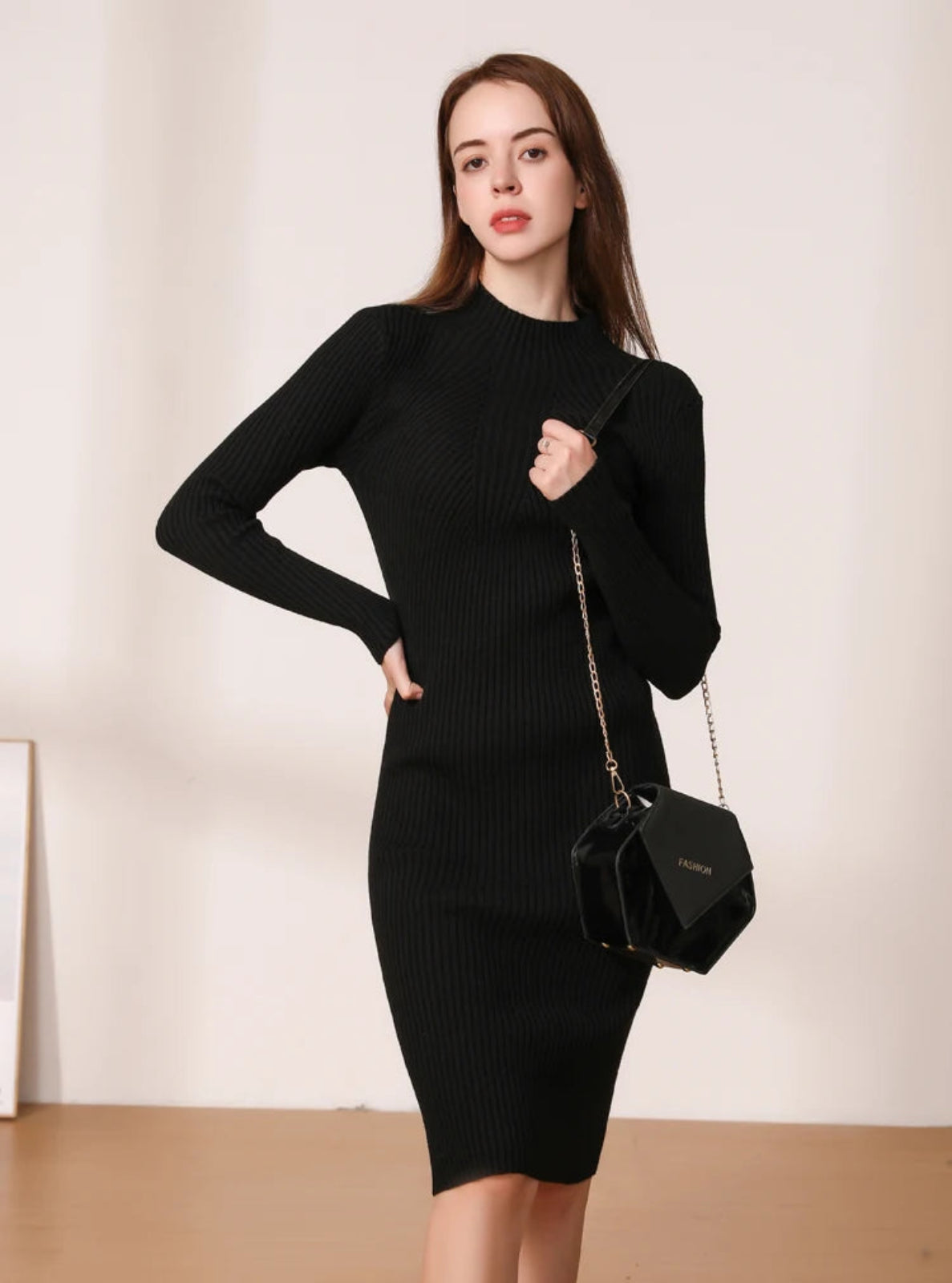 Woman wearing a black ribbed dress holding a matching black handbag against a plain background