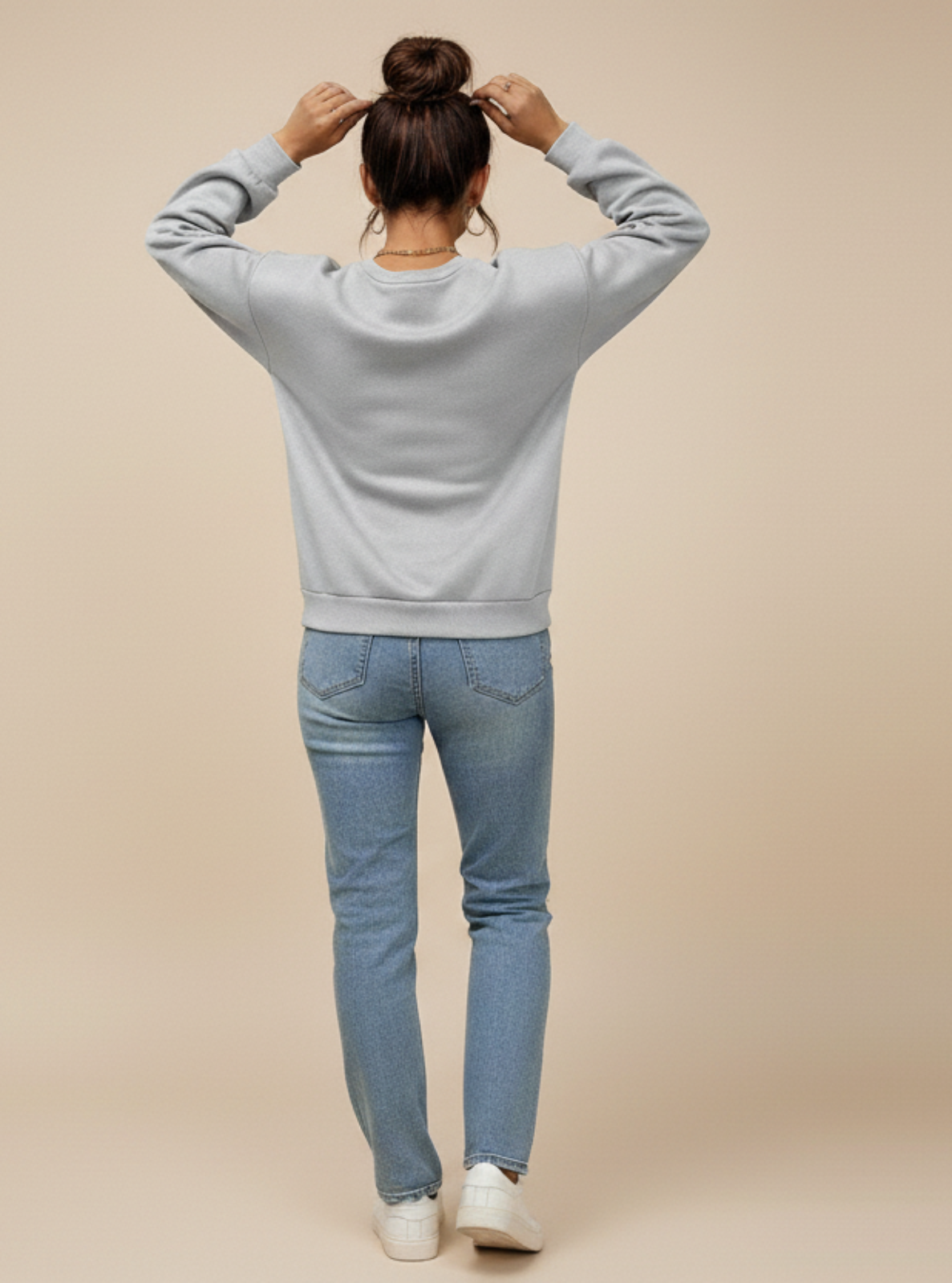 Person wearing a gray sweatshirt and blue jeans on a beige background