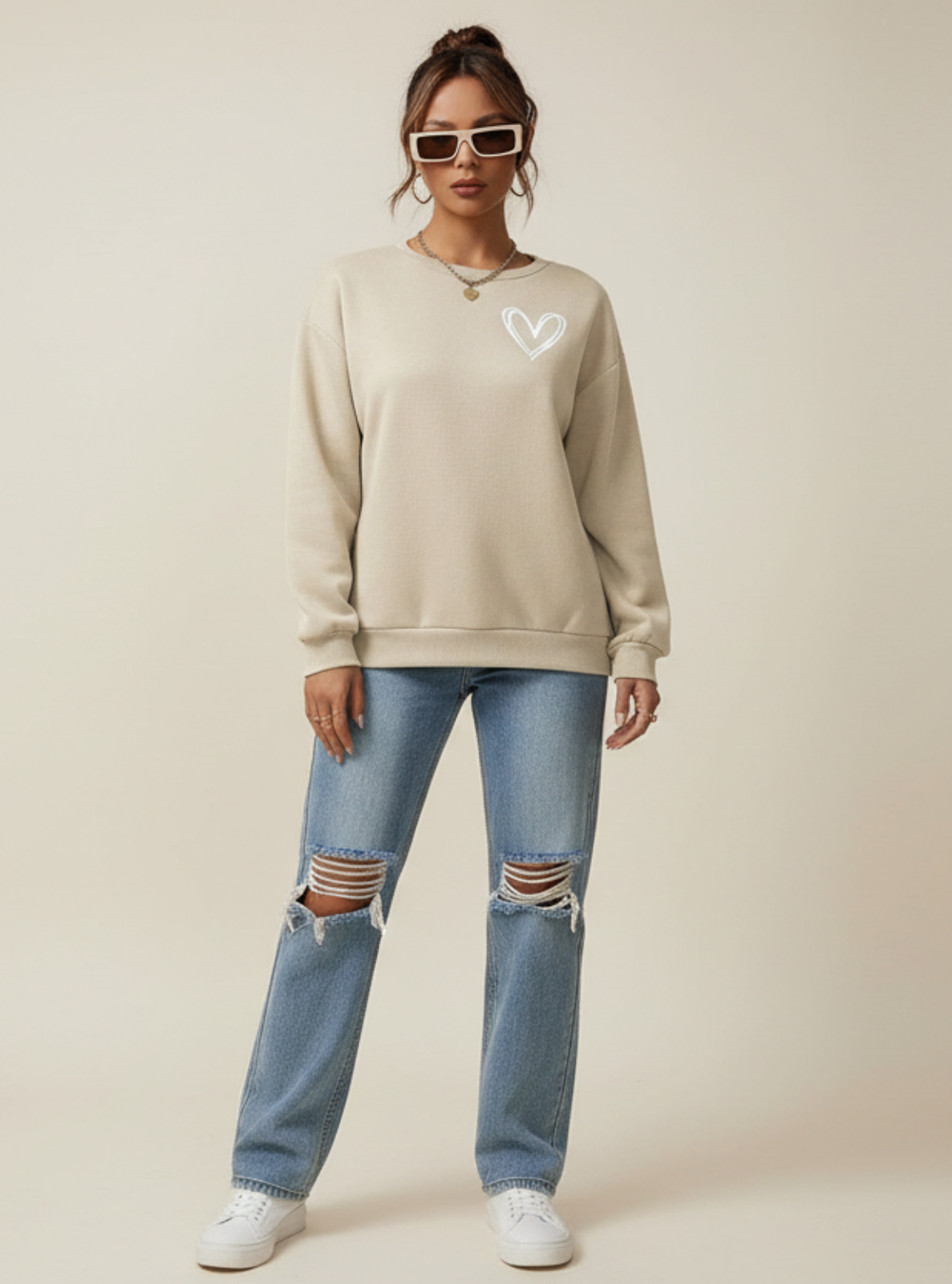 Person wearing a beige sweatshirt and ripped jeans on a plain background