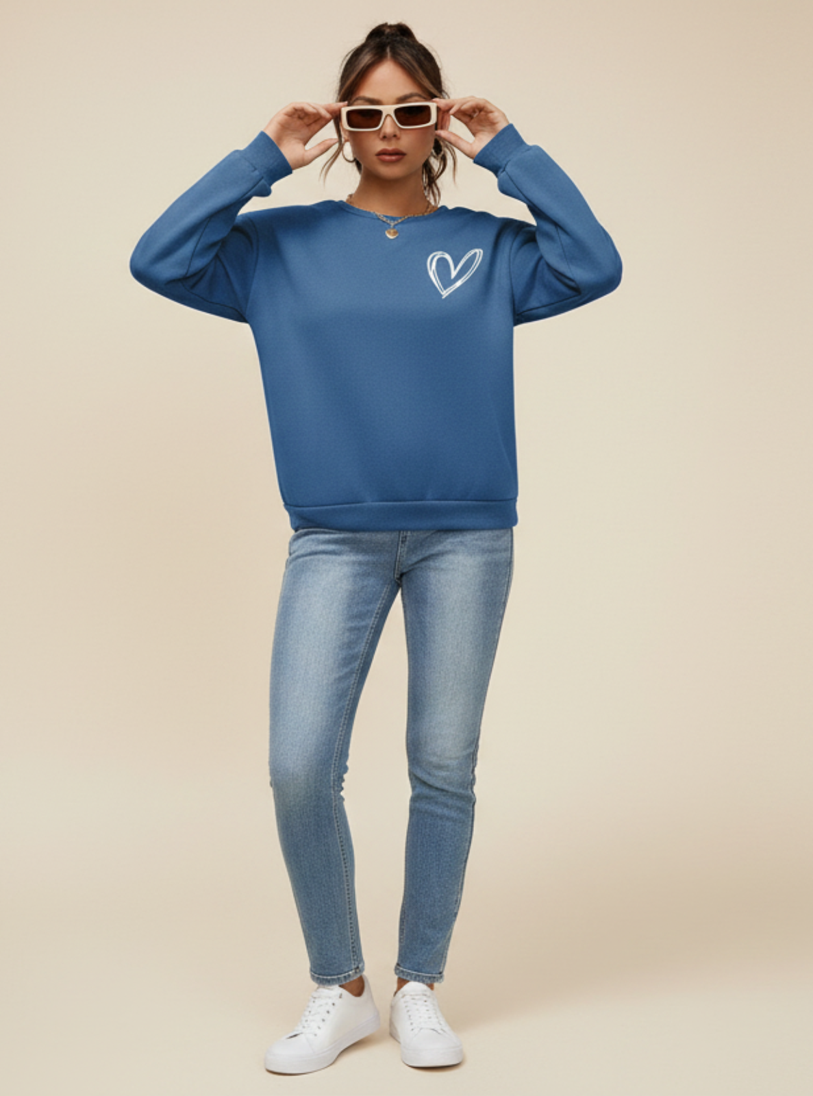 Woman wearing a blue sweatshirt with a heart design and sunglasses on a beige background