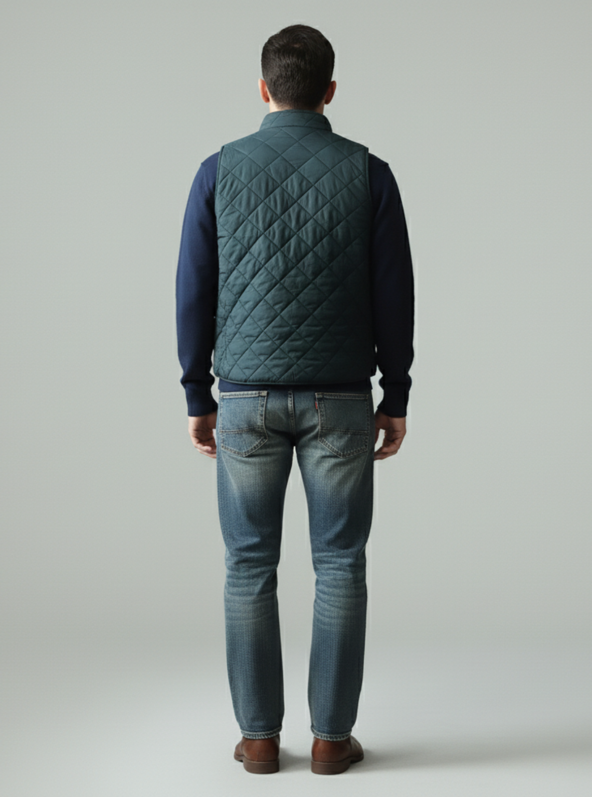 Man wearing a green quilted vest and blue jeans on a gray background