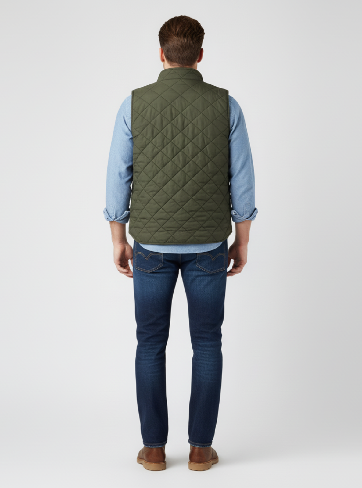 Man wearing a green quilted vest, blue jeans, and brown shoes on a white background