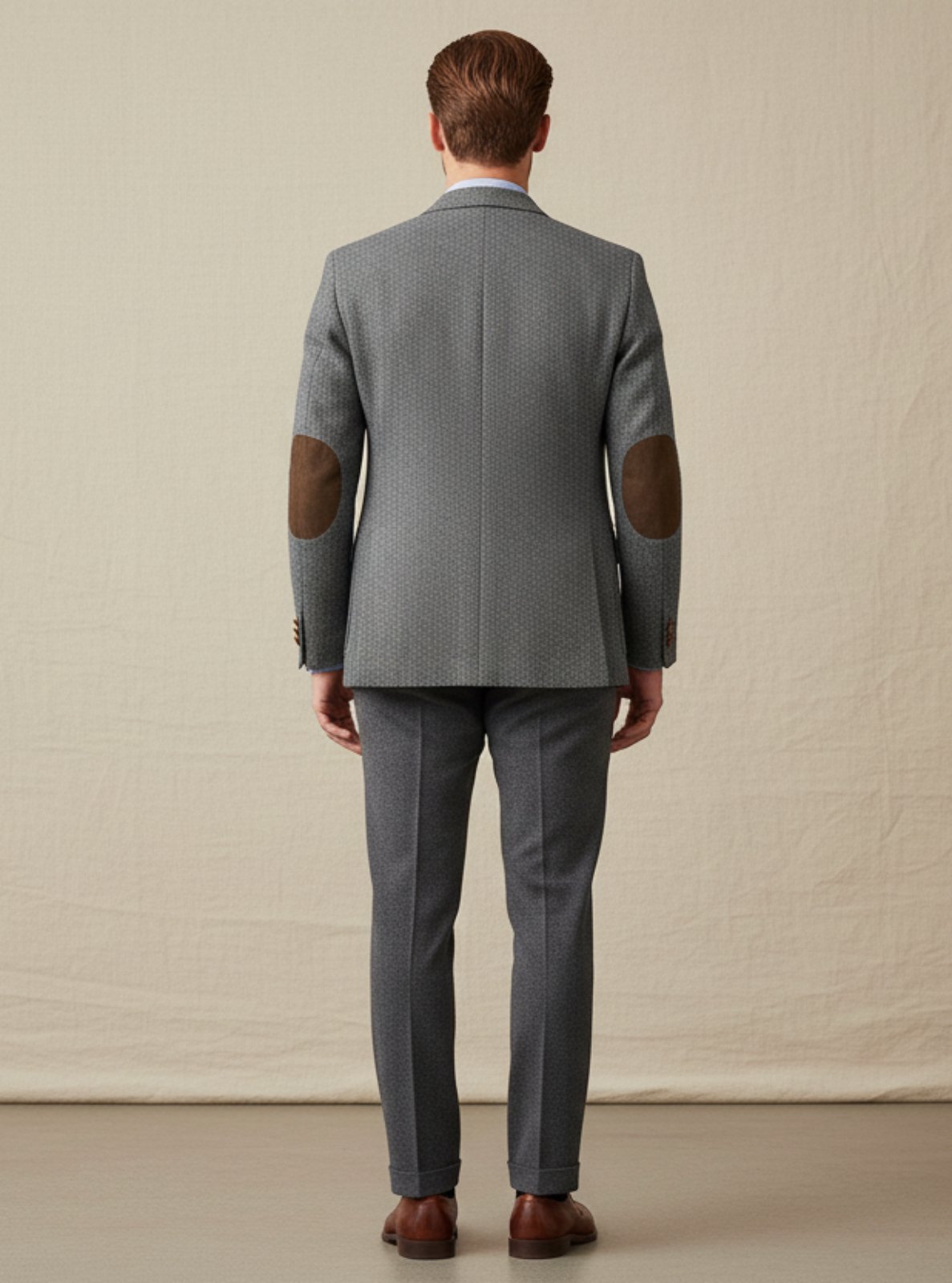 Man wearing a gray suit with elbow patches against a plain background