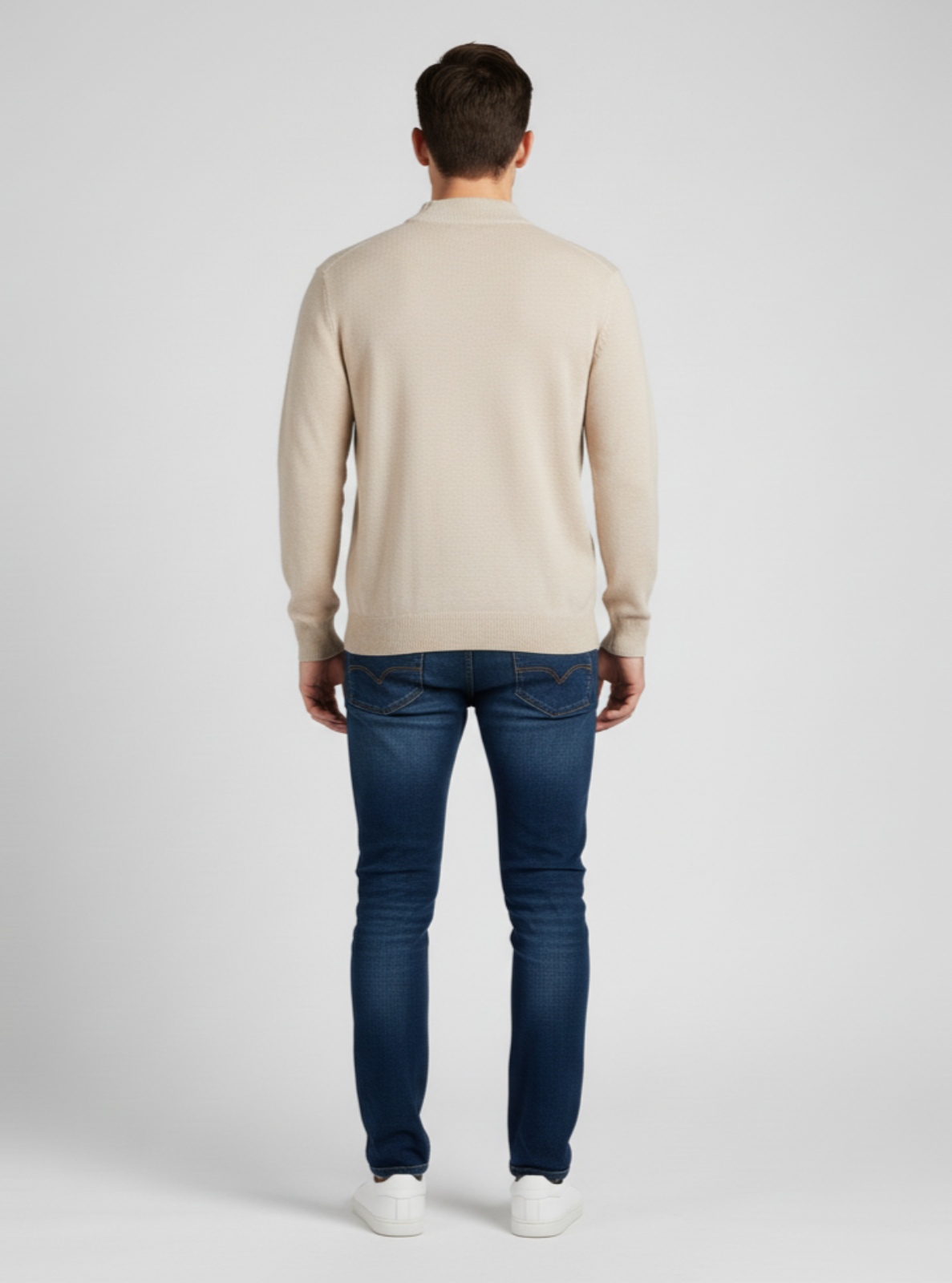 Man wearing a beige sweater and blue jeans on a white background