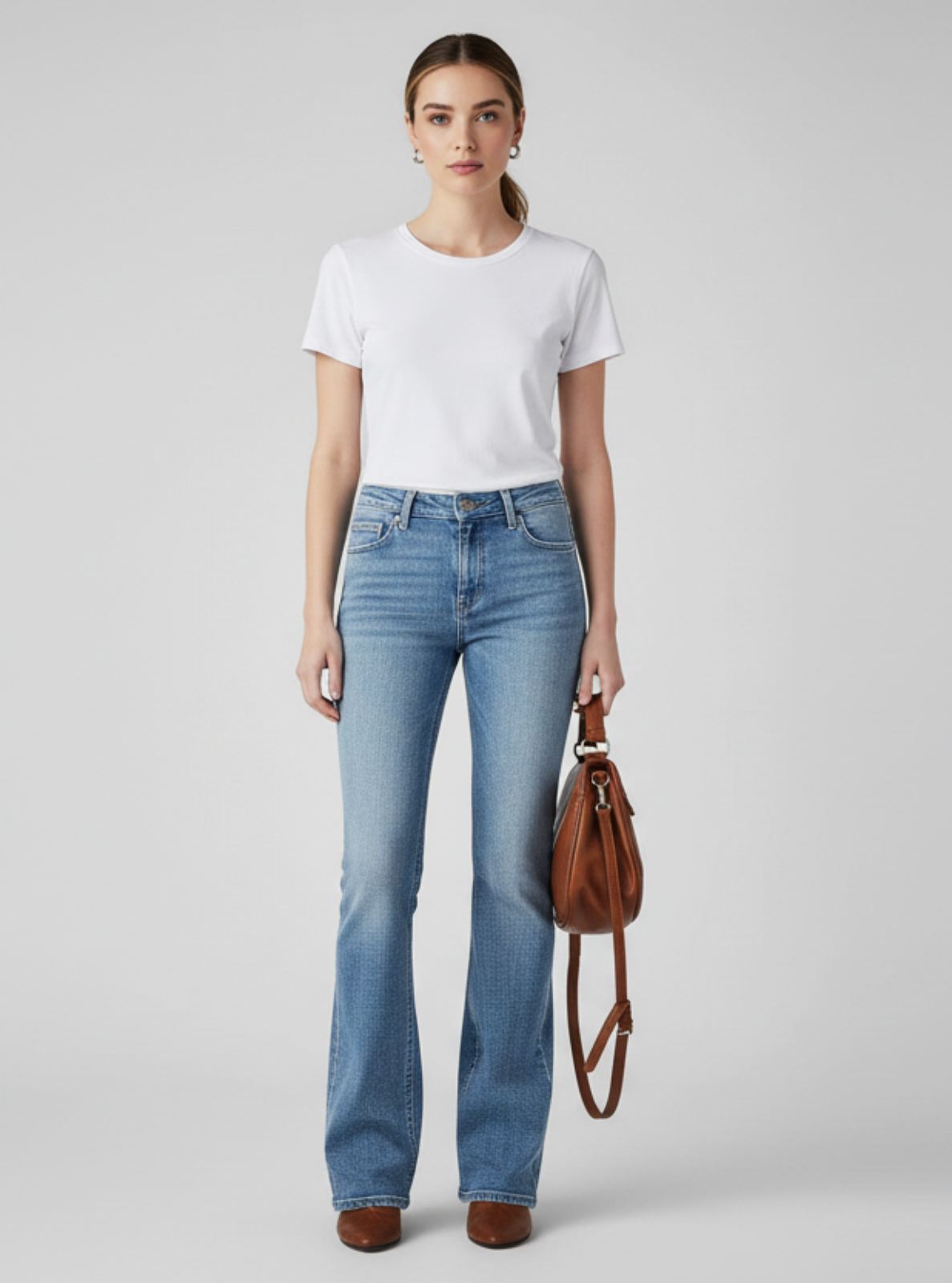 Woman wearing a white t-shirt and blue jeans holding a brown leather bag on a gray background
