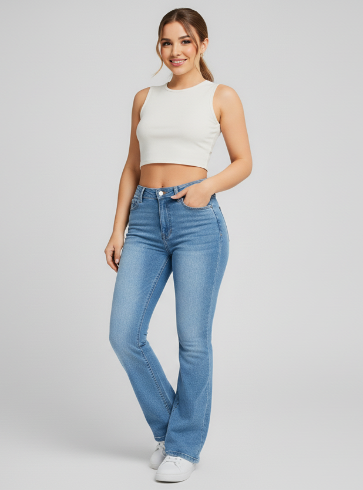 Woman wearing a white crop top and blue jeans on a plain background