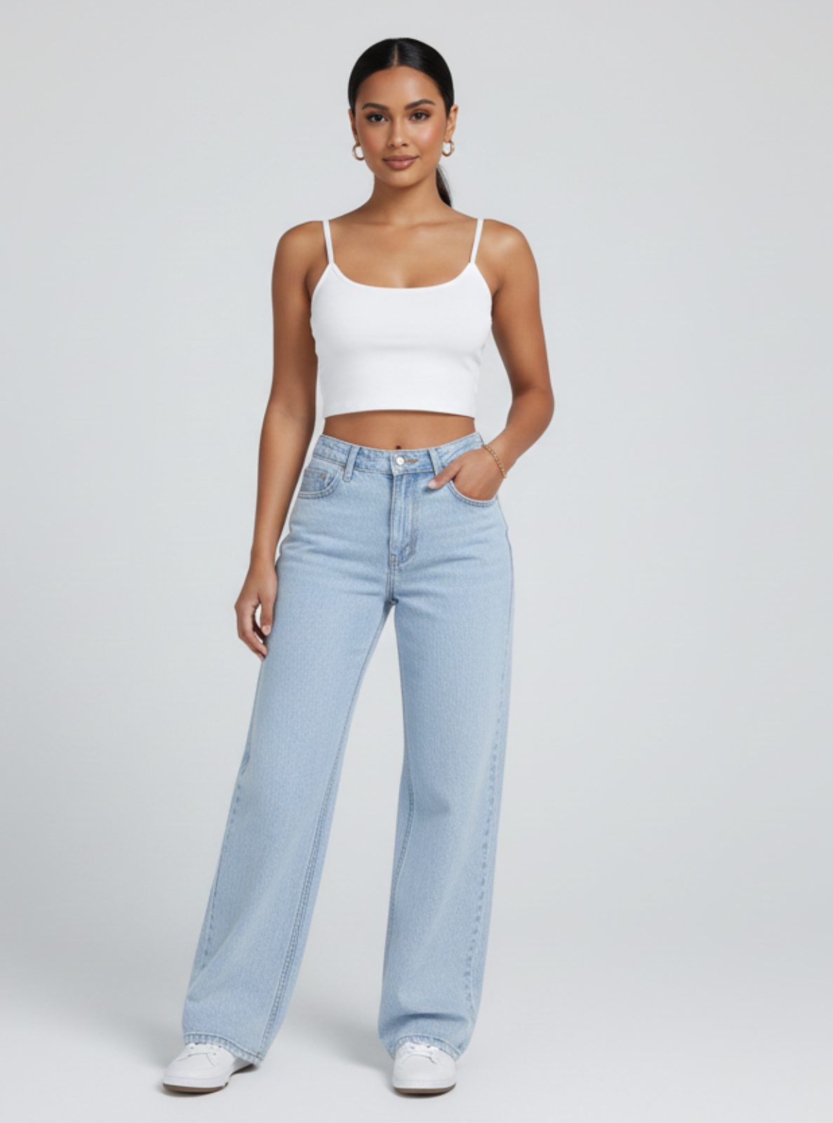 Woman wearing a white crop top and light blue jeans on a plain background