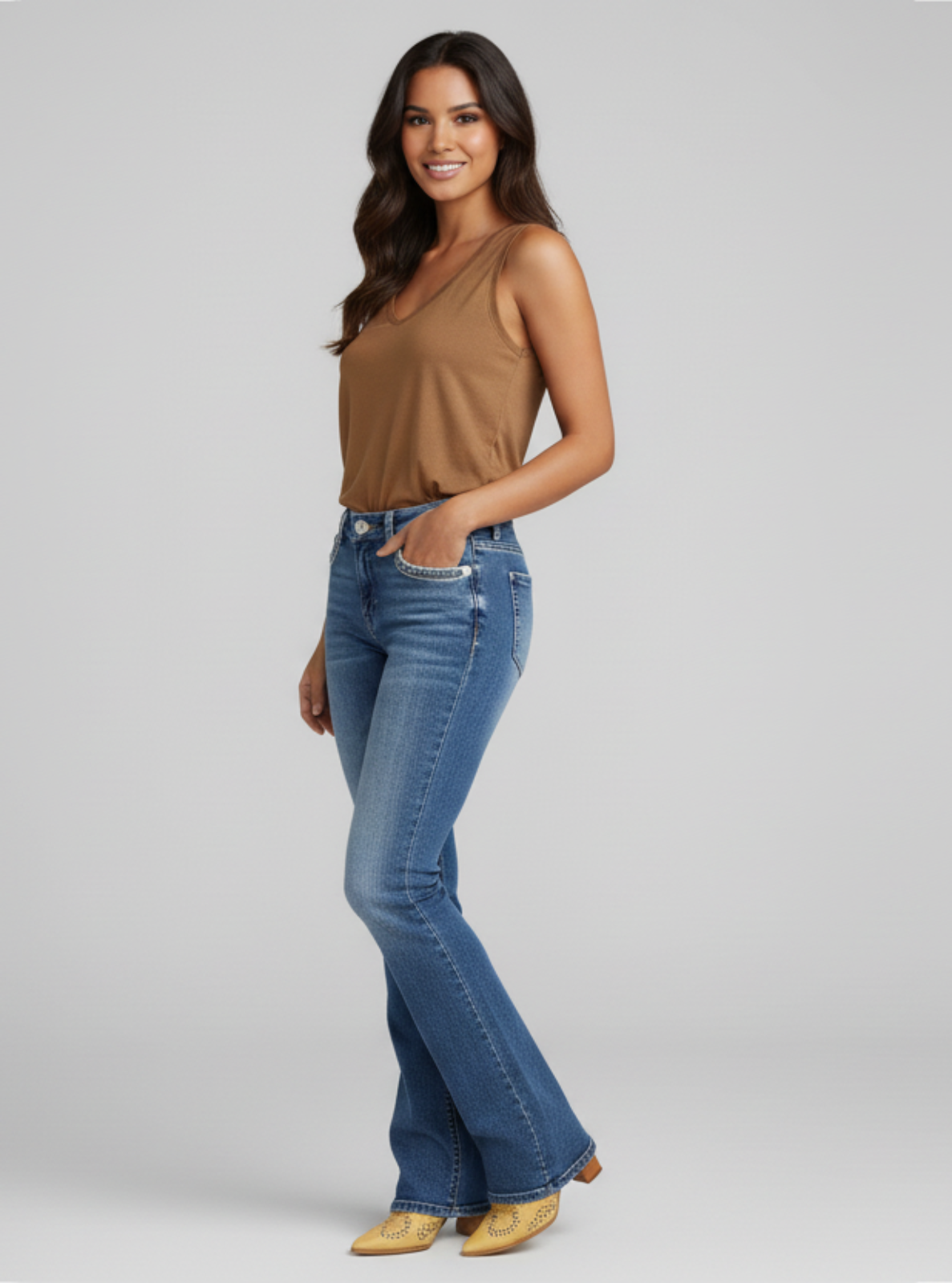 Woman wearing blue flared jeans and a brown top on a gray background