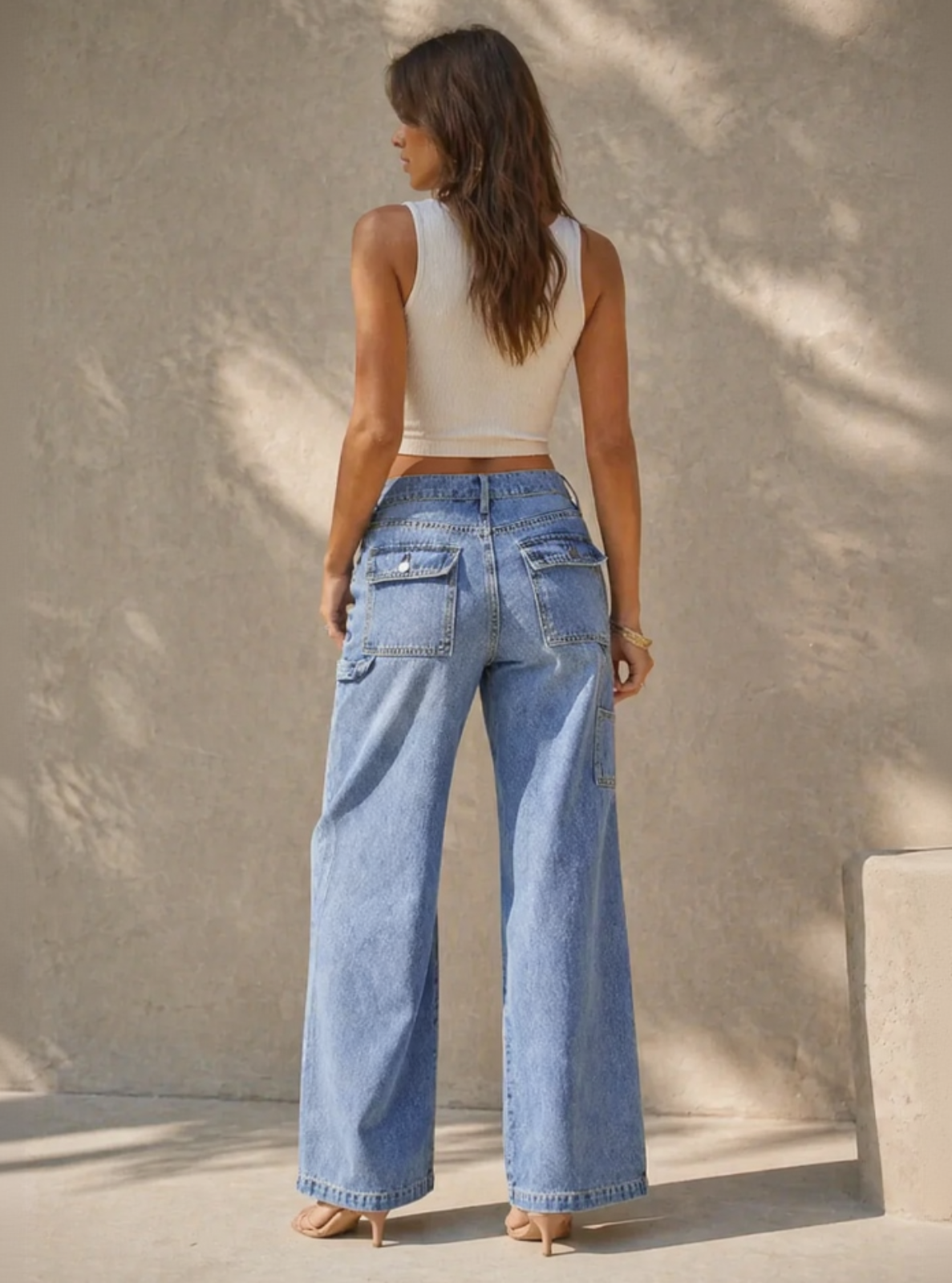 Woman wearing blue jeans and a white top standing against a textured wall.