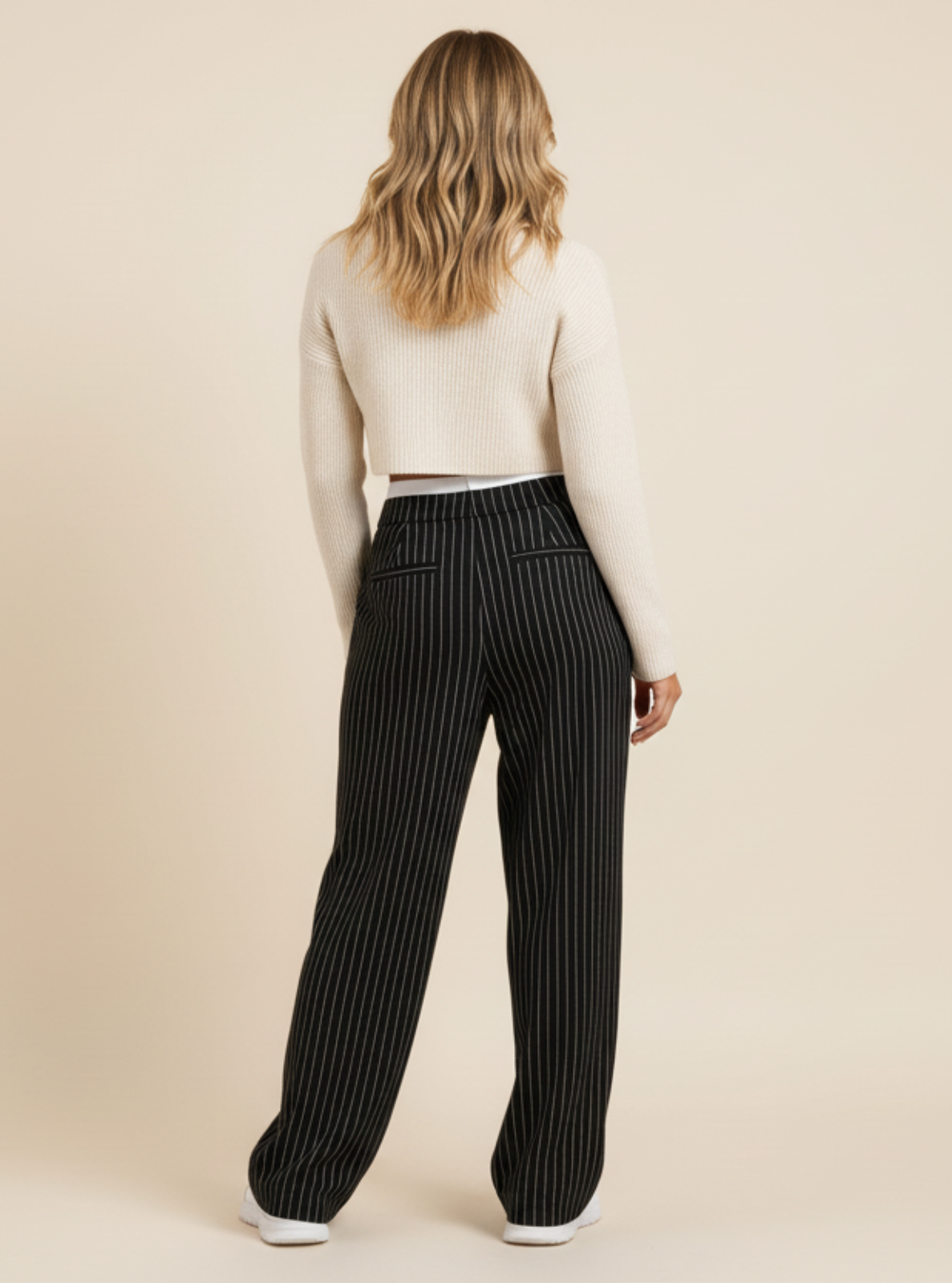 Person wearing a white long-sleeve top and black pinstripe pants on a beige background