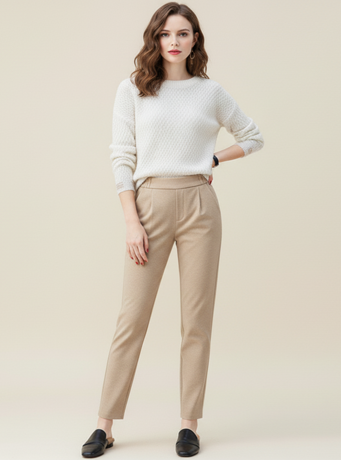 Woman wearing a white sweater and beige pants against a plain background