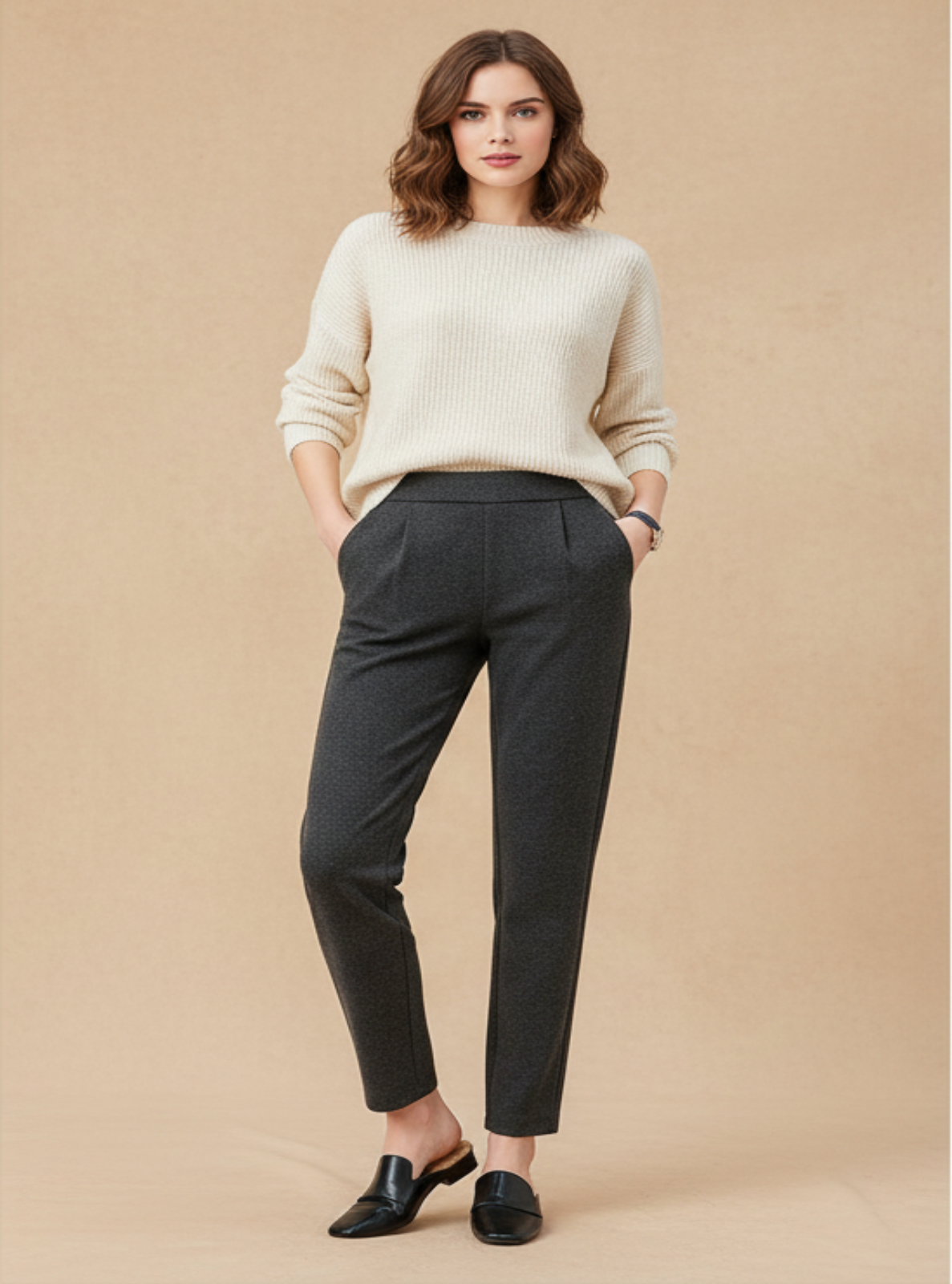 Woman wearing a beige sweater and dark gray pants on a beige background