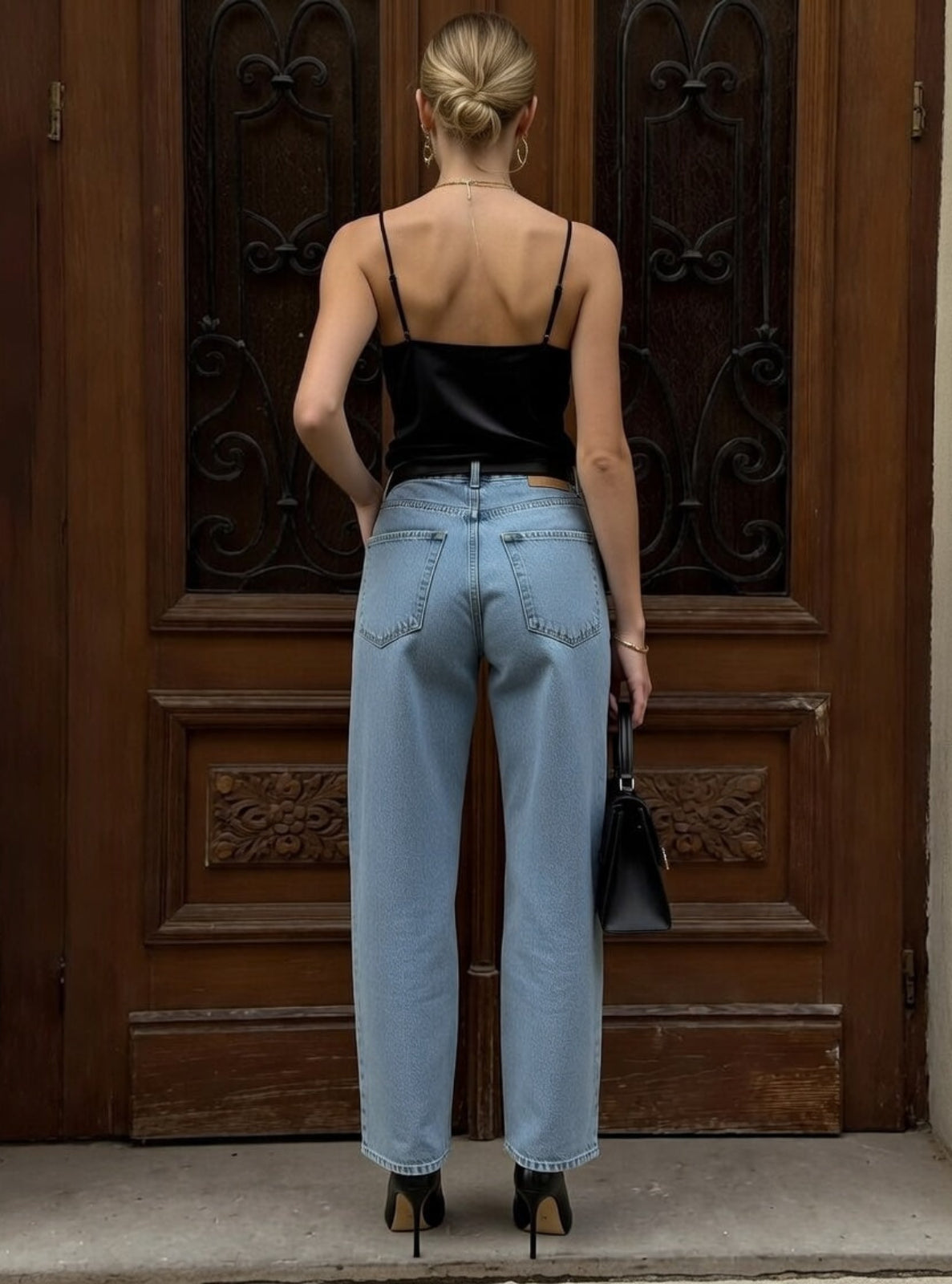 Woman wearing a black top and light blue jeans standing in front of a wooden door.