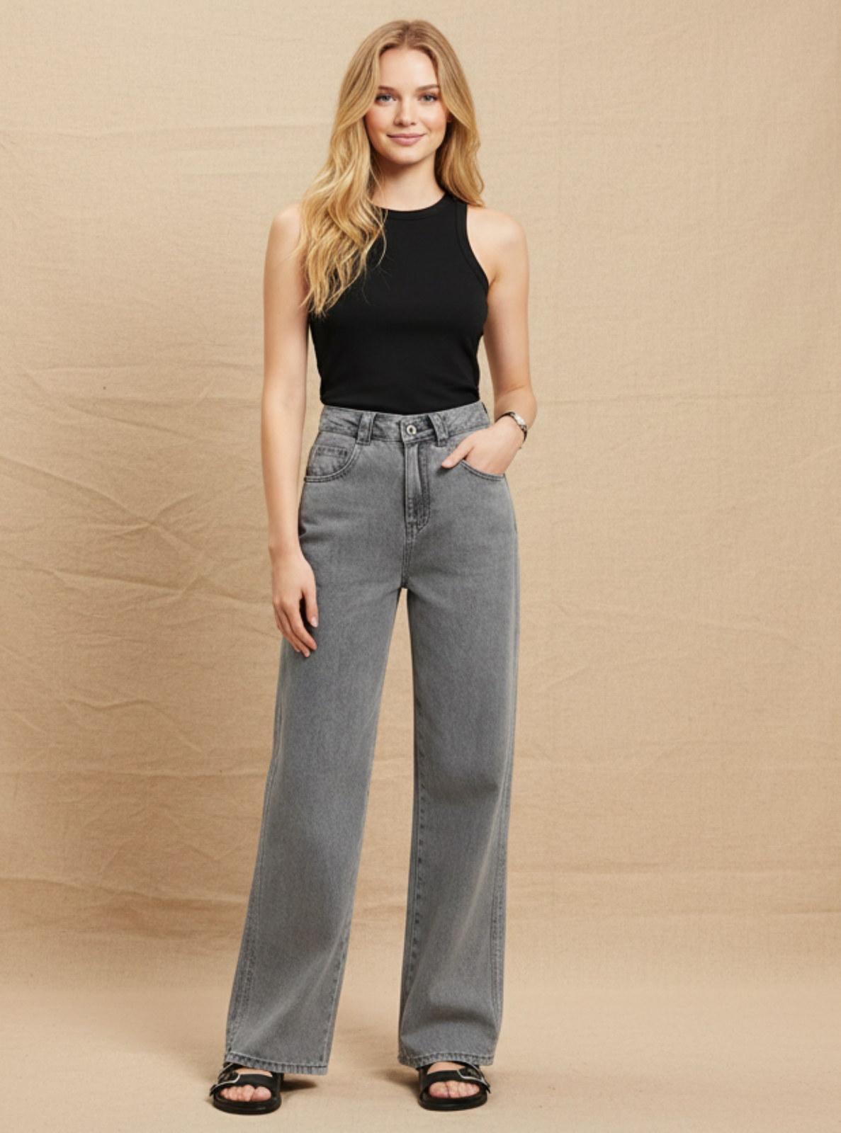 Woman wearing a black sleeveless top and gray high-waisted jeans against a beige background