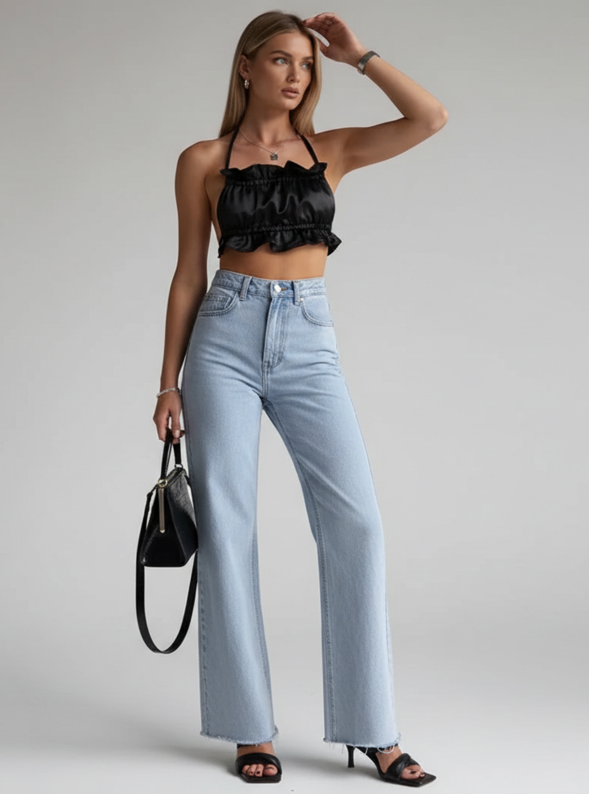 Woman wearing a black top and light blue jeans with a black handbag on a gray background