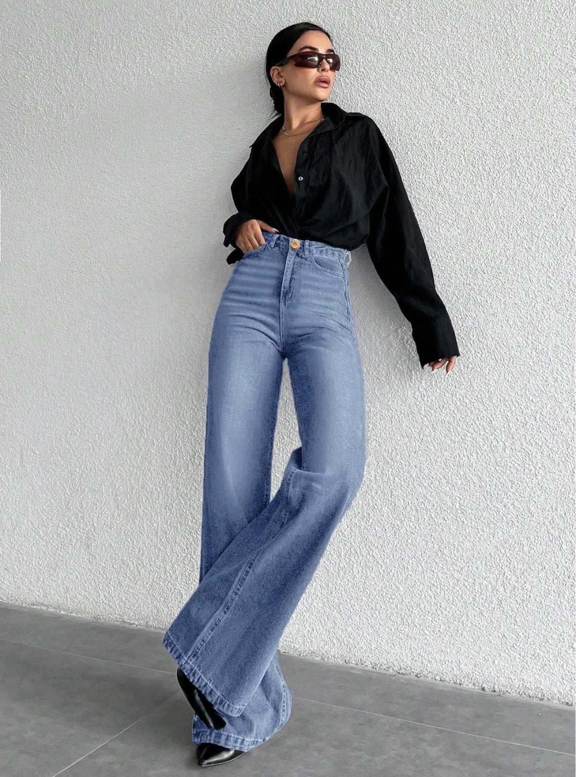 Person wearing black shirt and blue jeans against a white wall