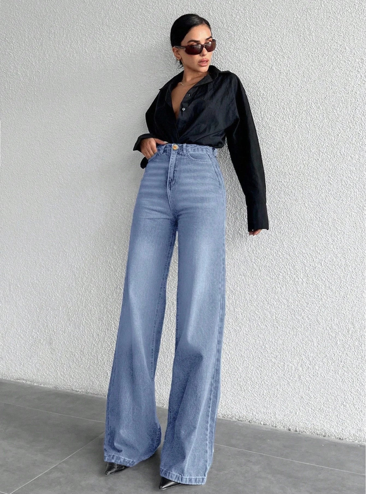 Woman wearing a black shirt and blue jeans against a white wall.