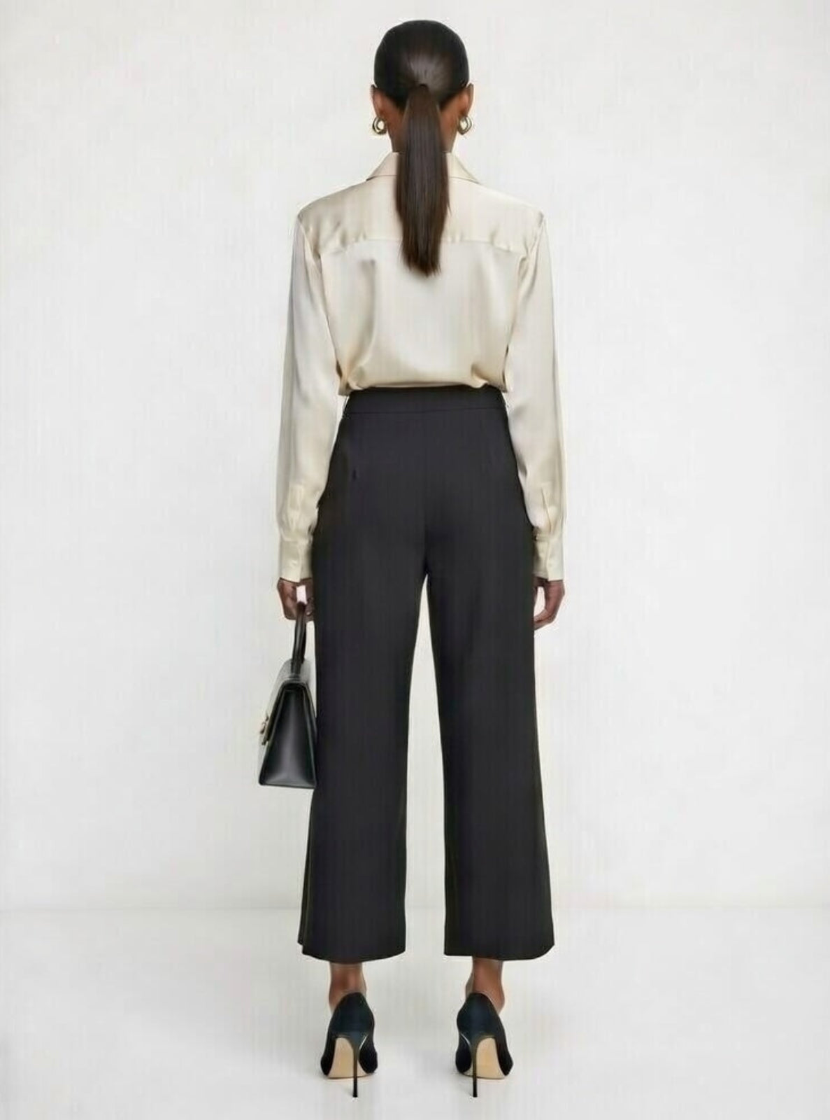 Person wearing a cream blouse and black pants on a white background