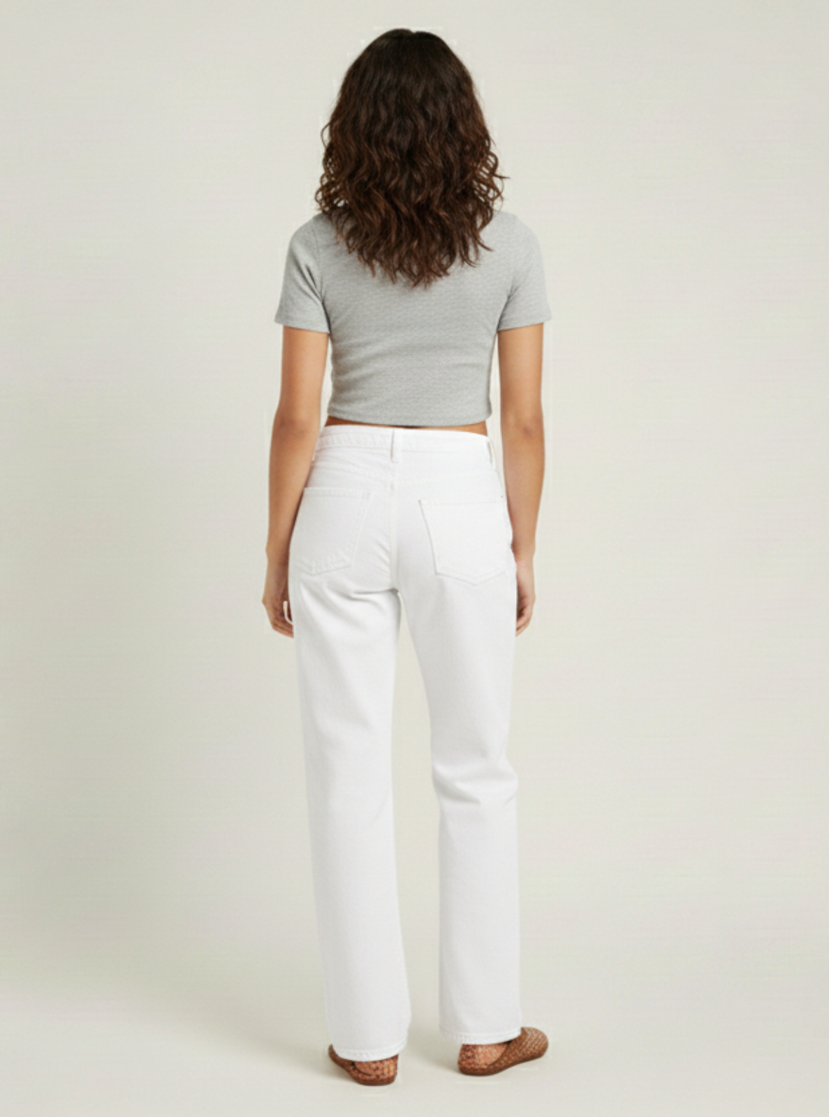 Woman wearing a light gray crop top and white pants on a plain background